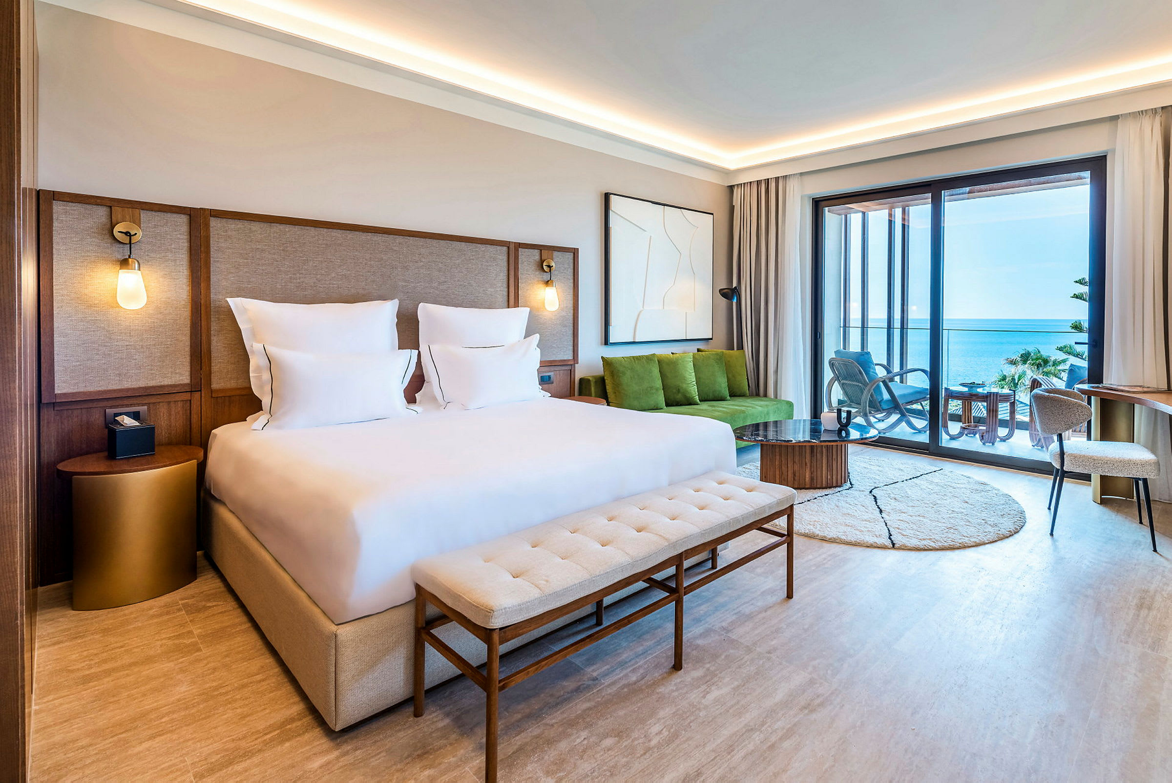 Ett modernt hotellrum med en dubbelsäng och utsikt över havet från en möblerad balkong. (AI-genererad text)