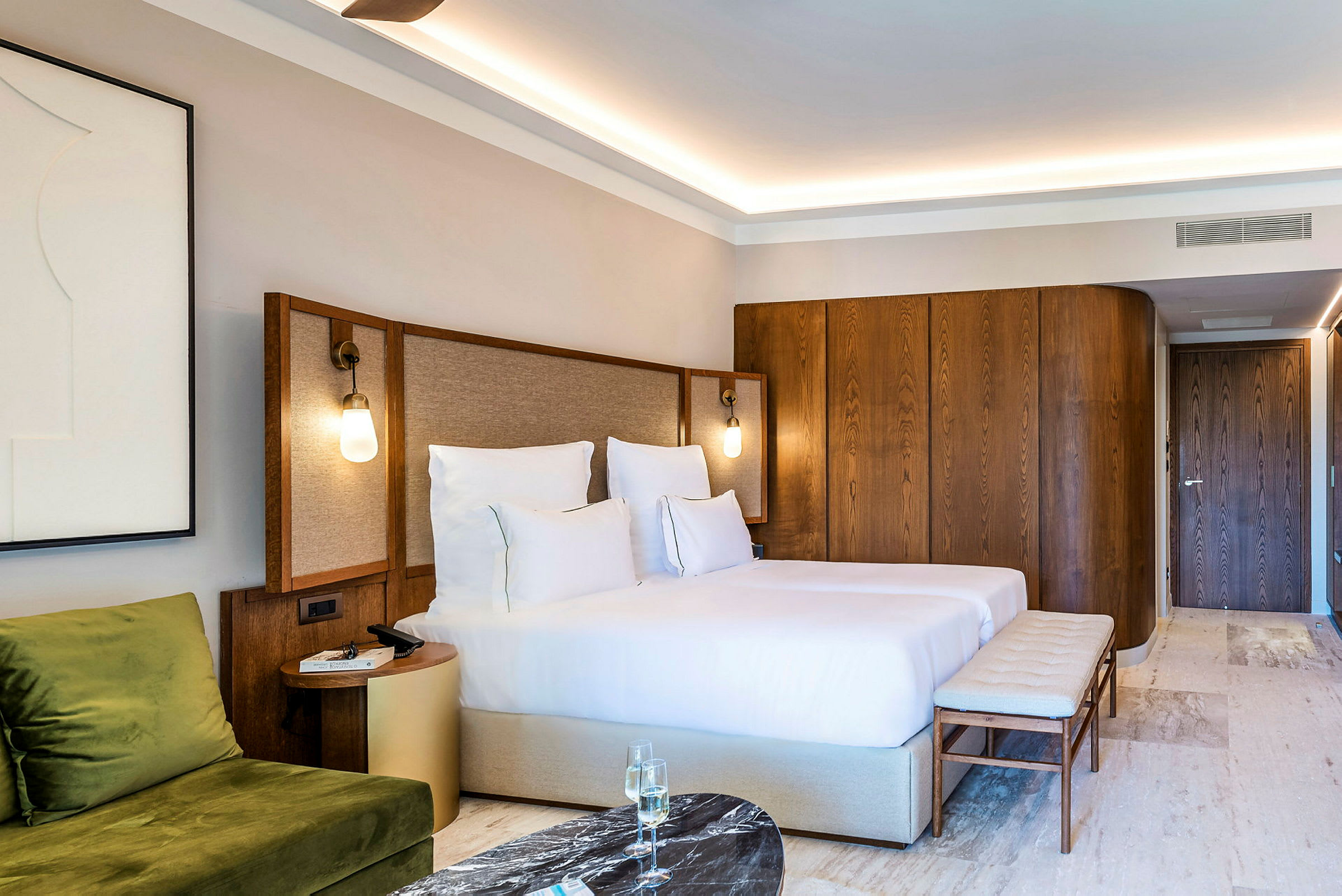 Hotellrum med en dubbelsäng, en sittplats med grön soffa, ett sidobord och inredning i trä. (AI-genererad text)