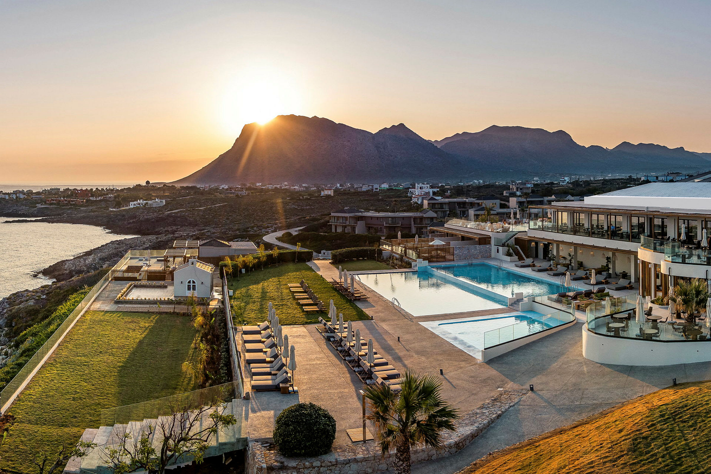 Solnedgång över hotellområde med pool, grönområden och omgivande bergslandskap. (AI-genererad text)