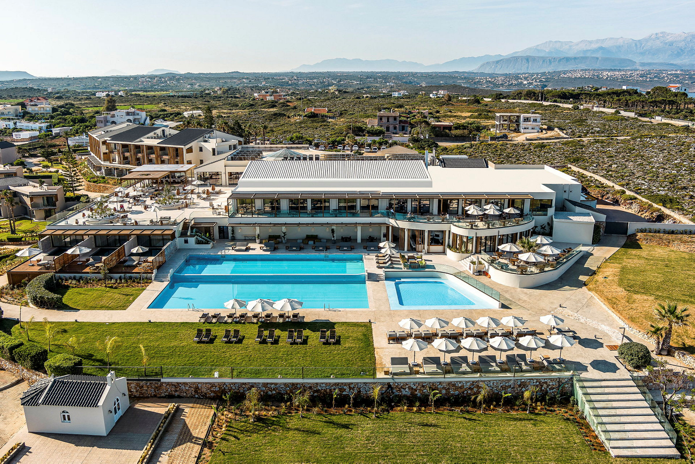 Flygfoto av en lyxig resort med poolområde, grönområden och omgivande landskap. (AI-genererad text)