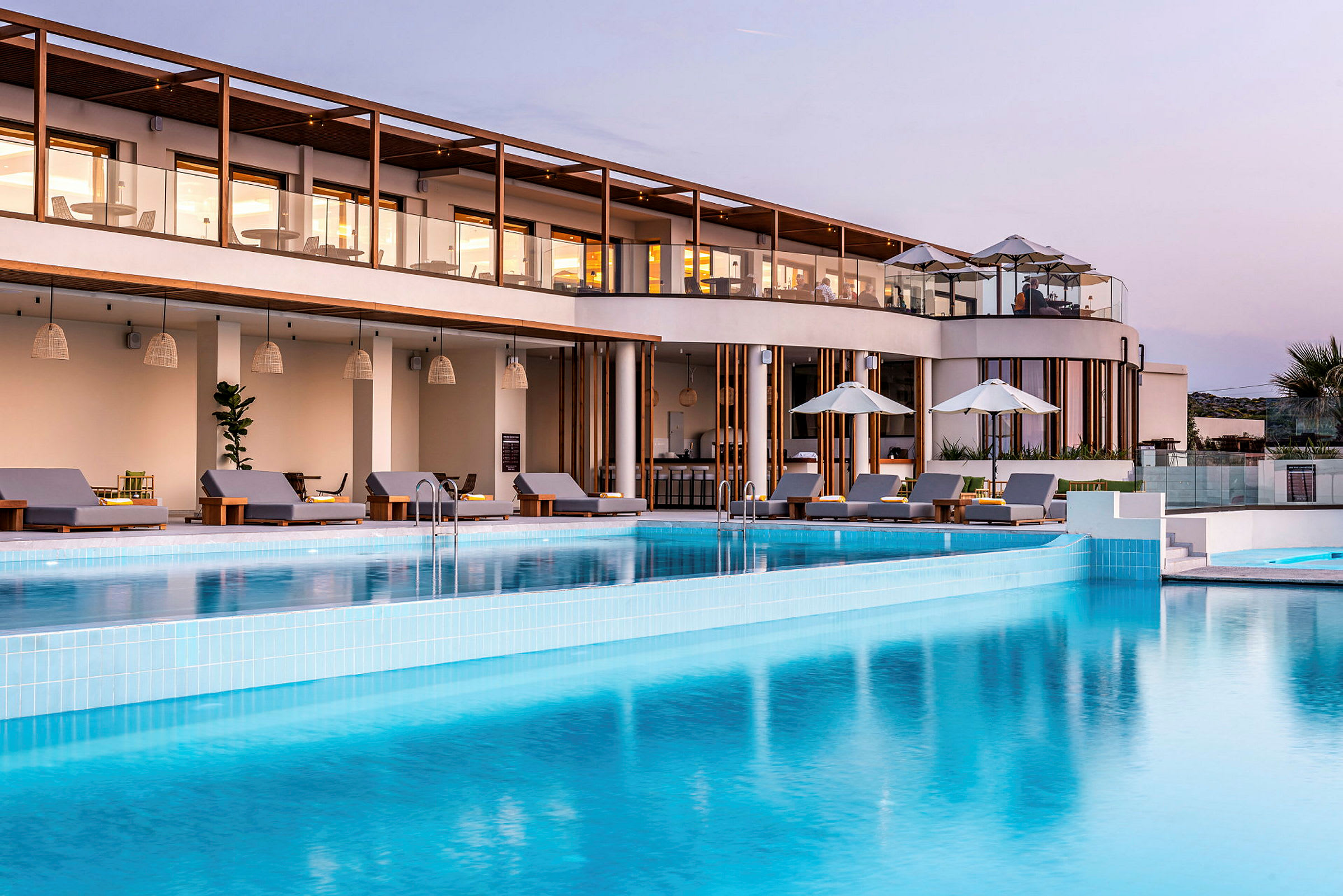 Bild av en modern semesteranläggning med en pool framför byggnaden. Solstolar och parasoll är placerade runt poolområdet. (AI-genererad text)