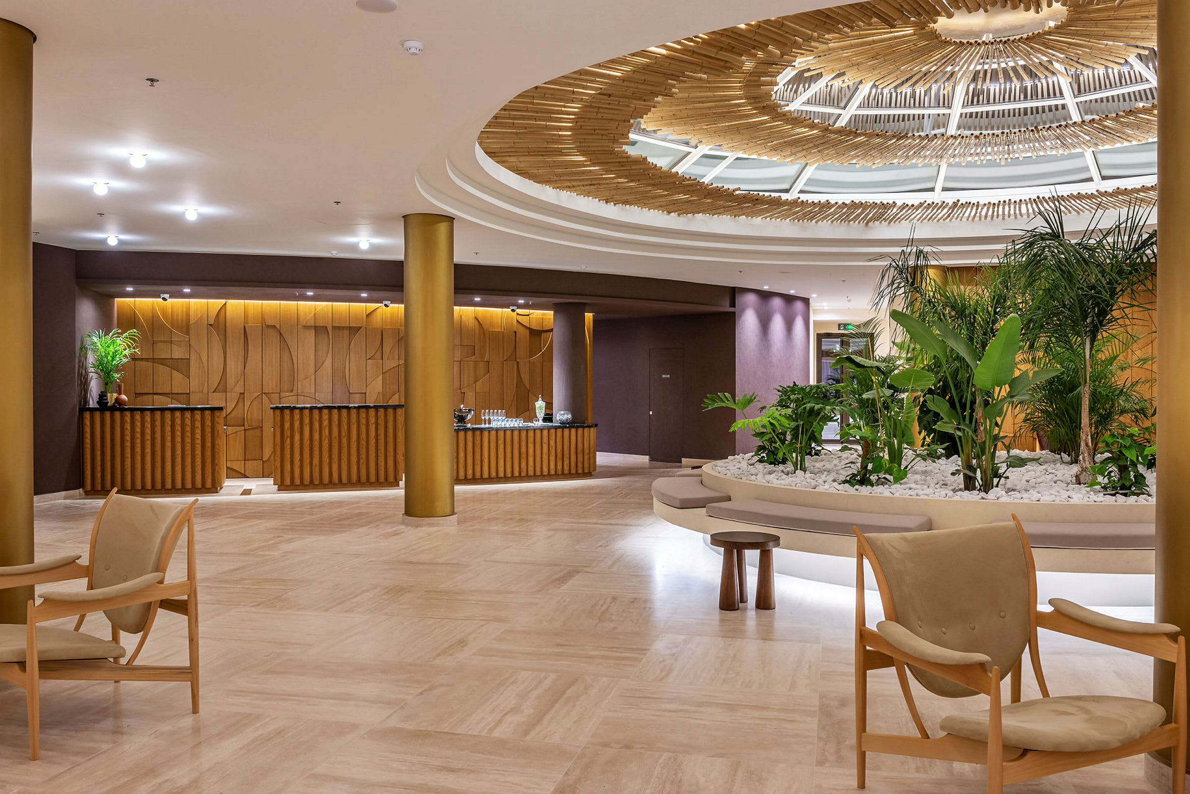 Ett hotellobbyområde med elegant inredning, inklusive gröna växter, sittmöbler och en dekorativ takkonstruktion. (AI-genererad text)