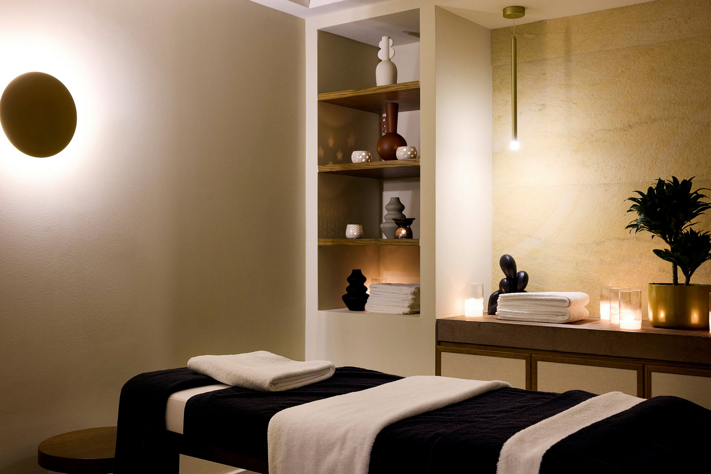 Ett spa-rum med massagebord, hyllor med dekorationer och handdukar samt mjuk belysning. (AI-genererad text)