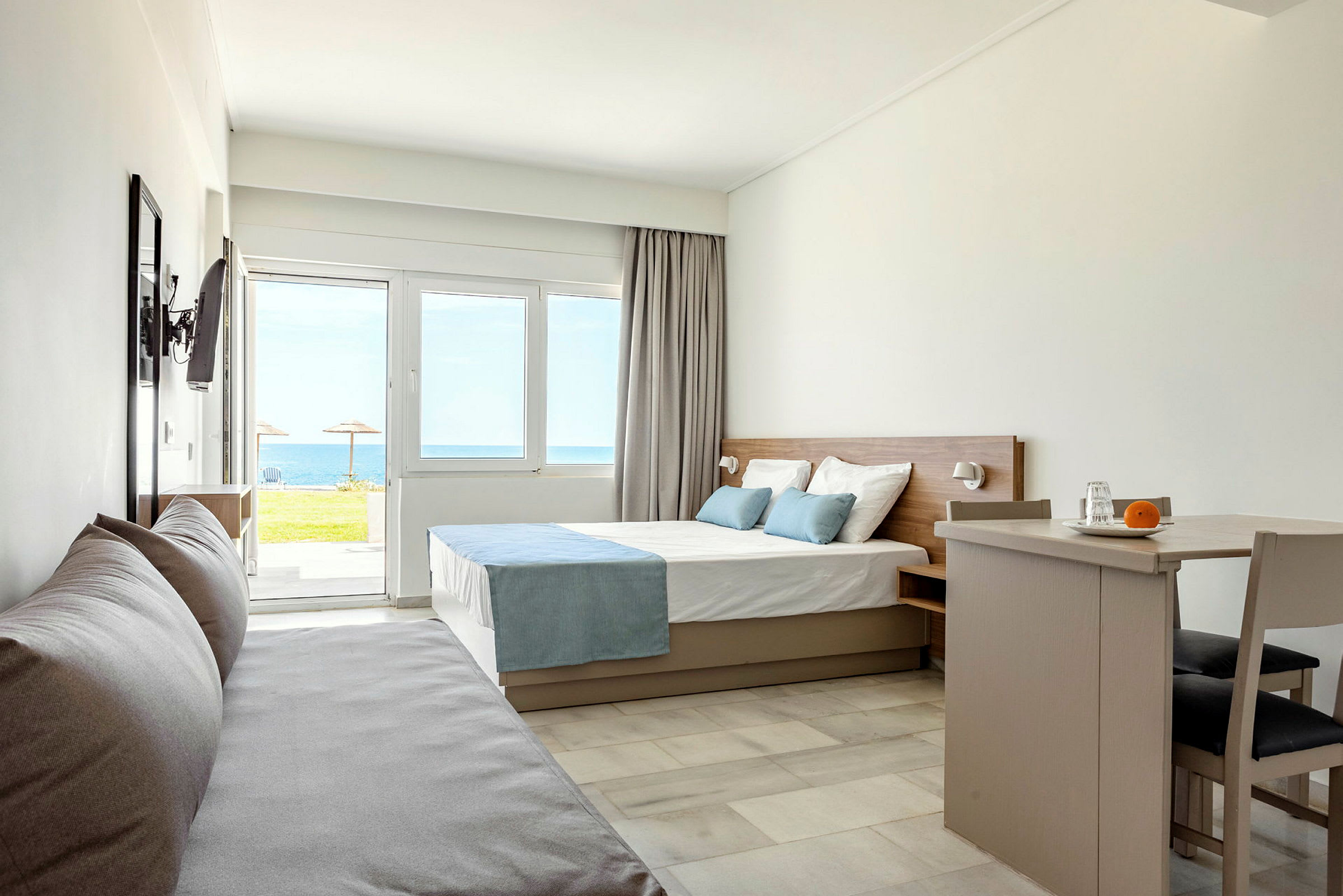 Modernt hotellrum med säng, soffa och matbord, havsutsikt utanför fönstret. (AI-genererad text)