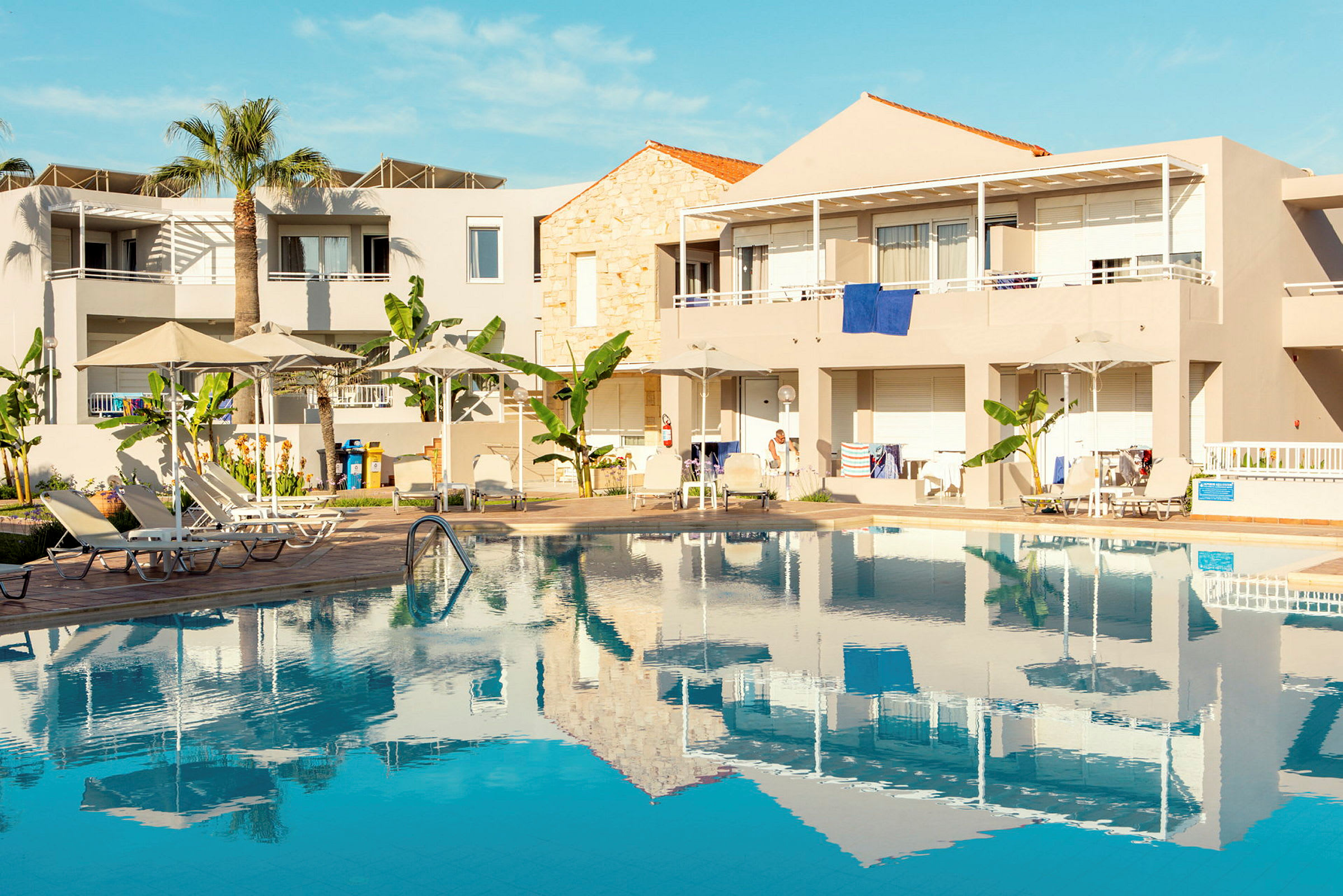 Lägenhetshotell med pool och solstolar under parasoll. (AI-genererad text)