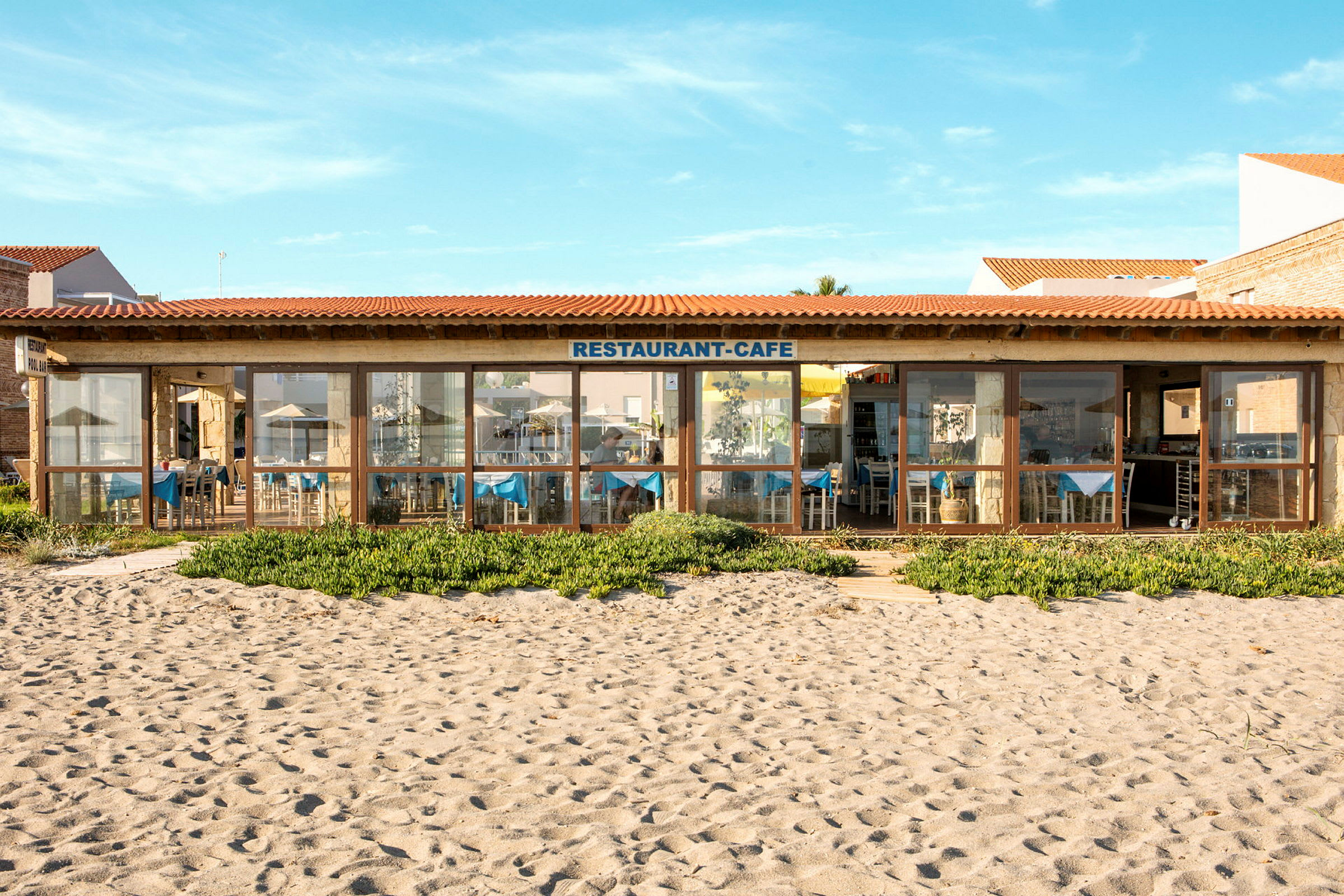 En restaurang med glasfasad med utsikt över sandstrand och grönska. (AI-genererad text)