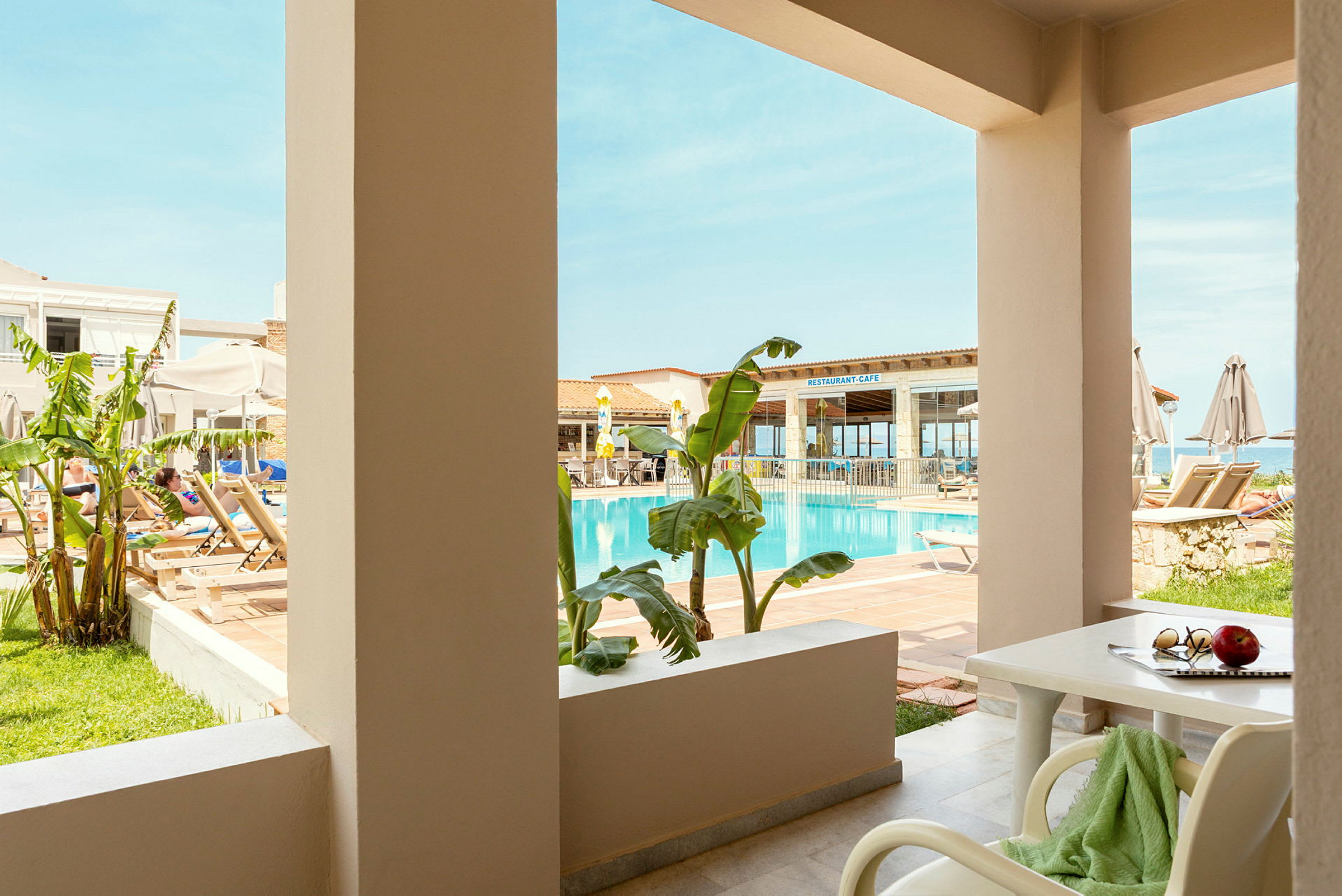 Bild som visar en terrass med utsikt mot en pool och en restaurang i bakgrunden. (AI-genererad text)