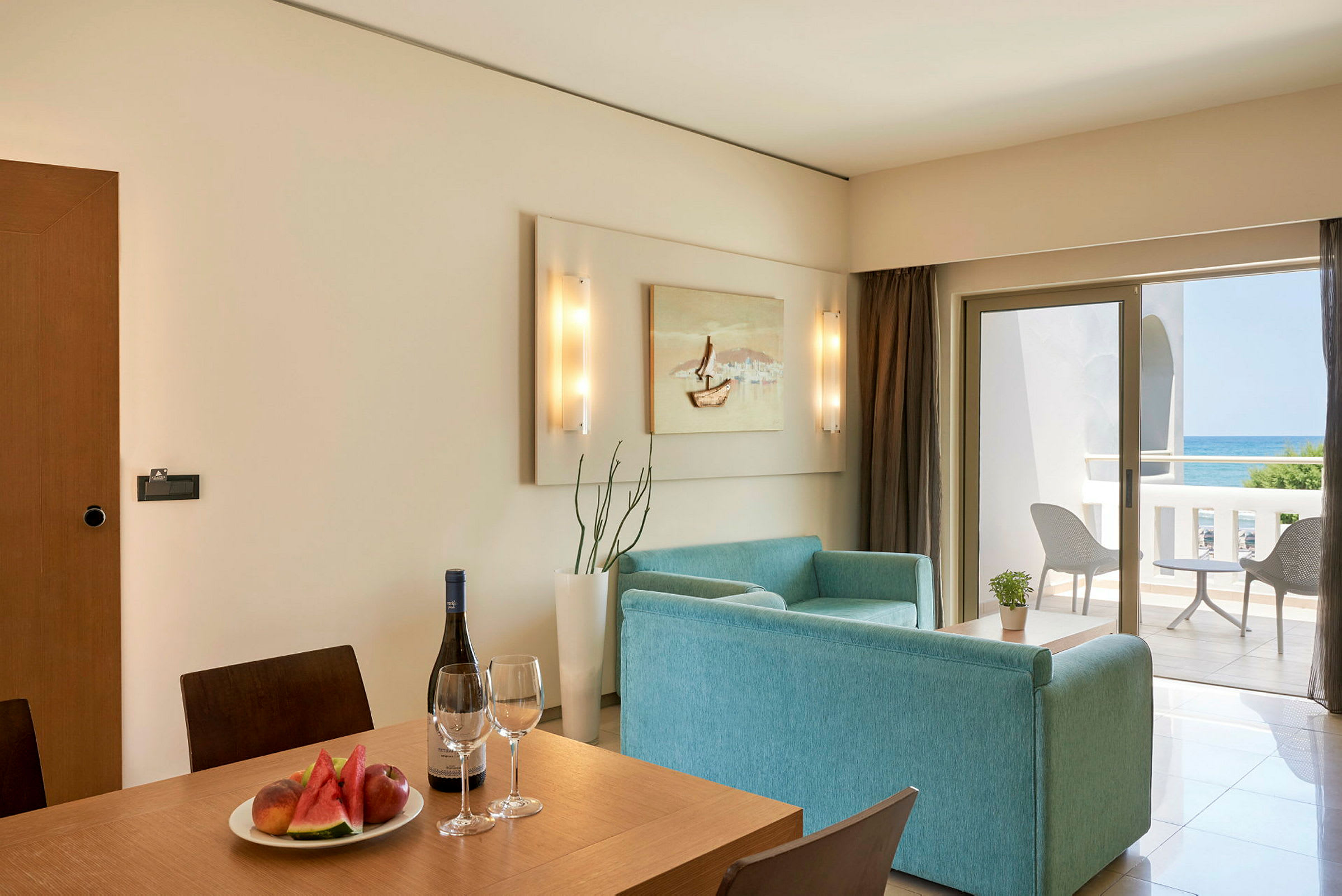 Ett hotellrum med matplats och sittgrupp, samt en balkong med havsutsikt. (AI-genererad text)