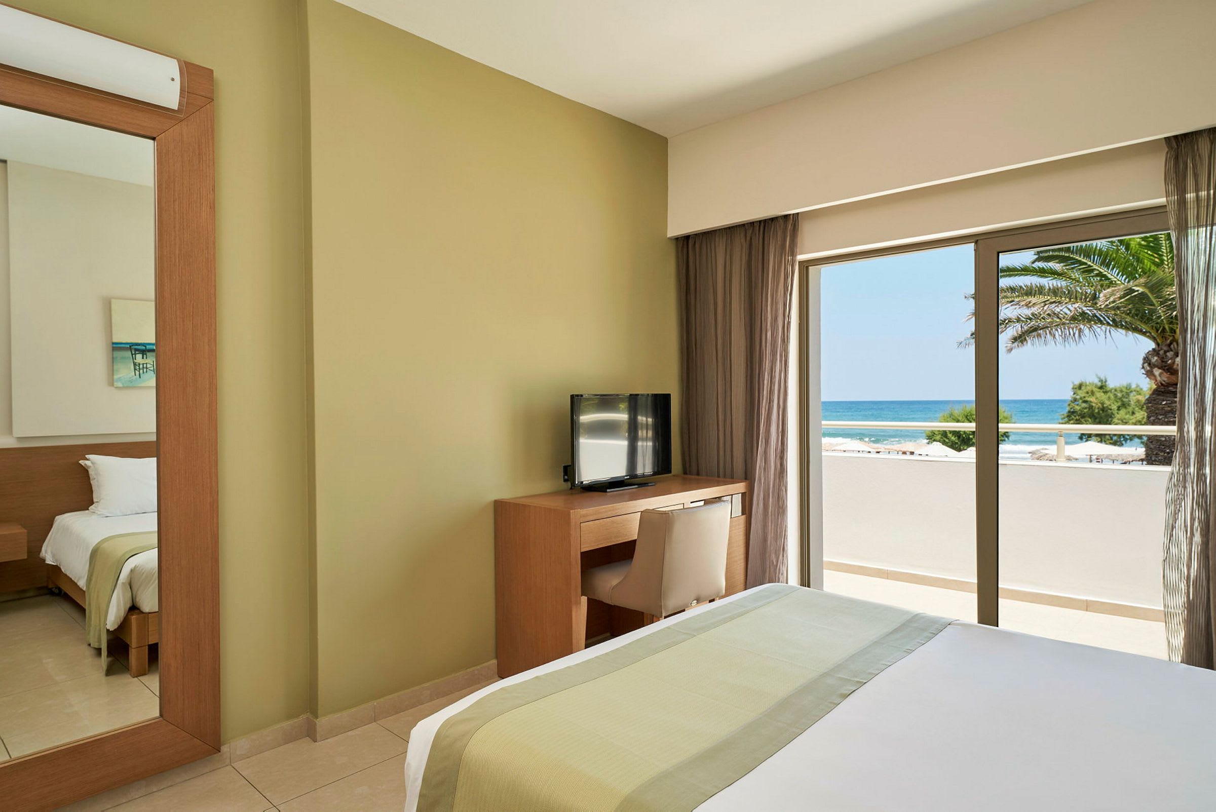 Hotellrum med säng, TV och skrivbord samt utsikt över havet genom ett fönster. (AI-genererad text)