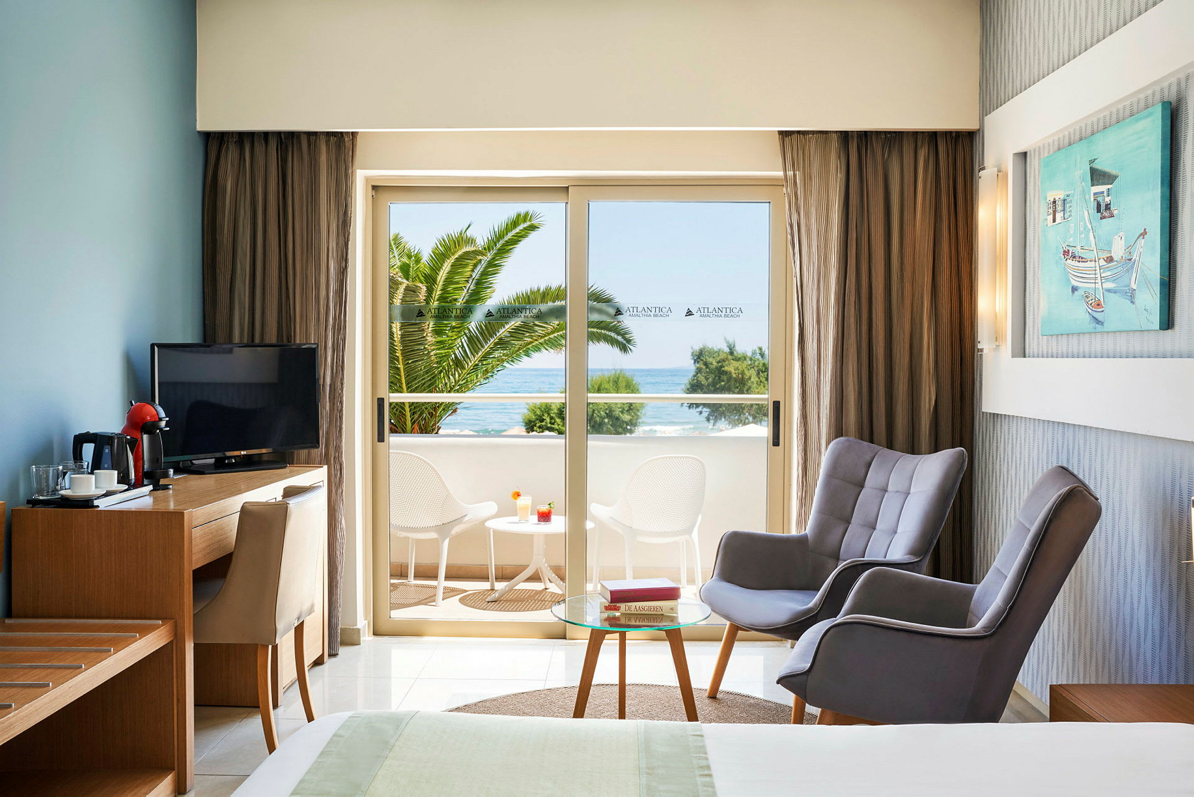 Hotellrum med sittgrupp och utsikt mot balkong med bord och stolar samt havsutsikt. (AI-genererad text)