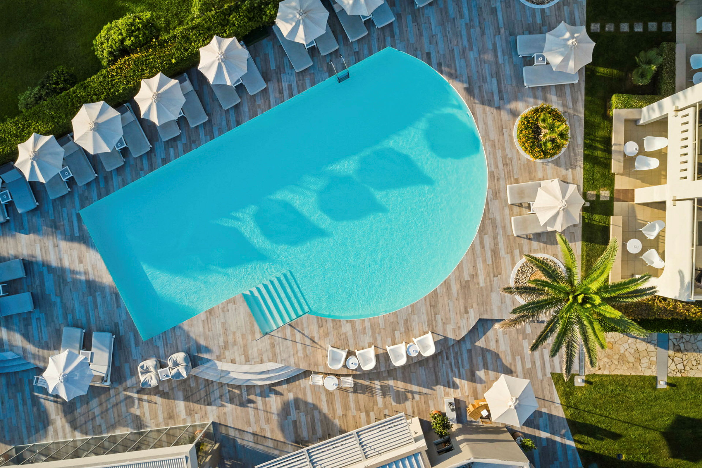 Flygfoto över en pool, solstolar och parasoller samt grönska i ett semesterkomplex. (AI-genererad text)