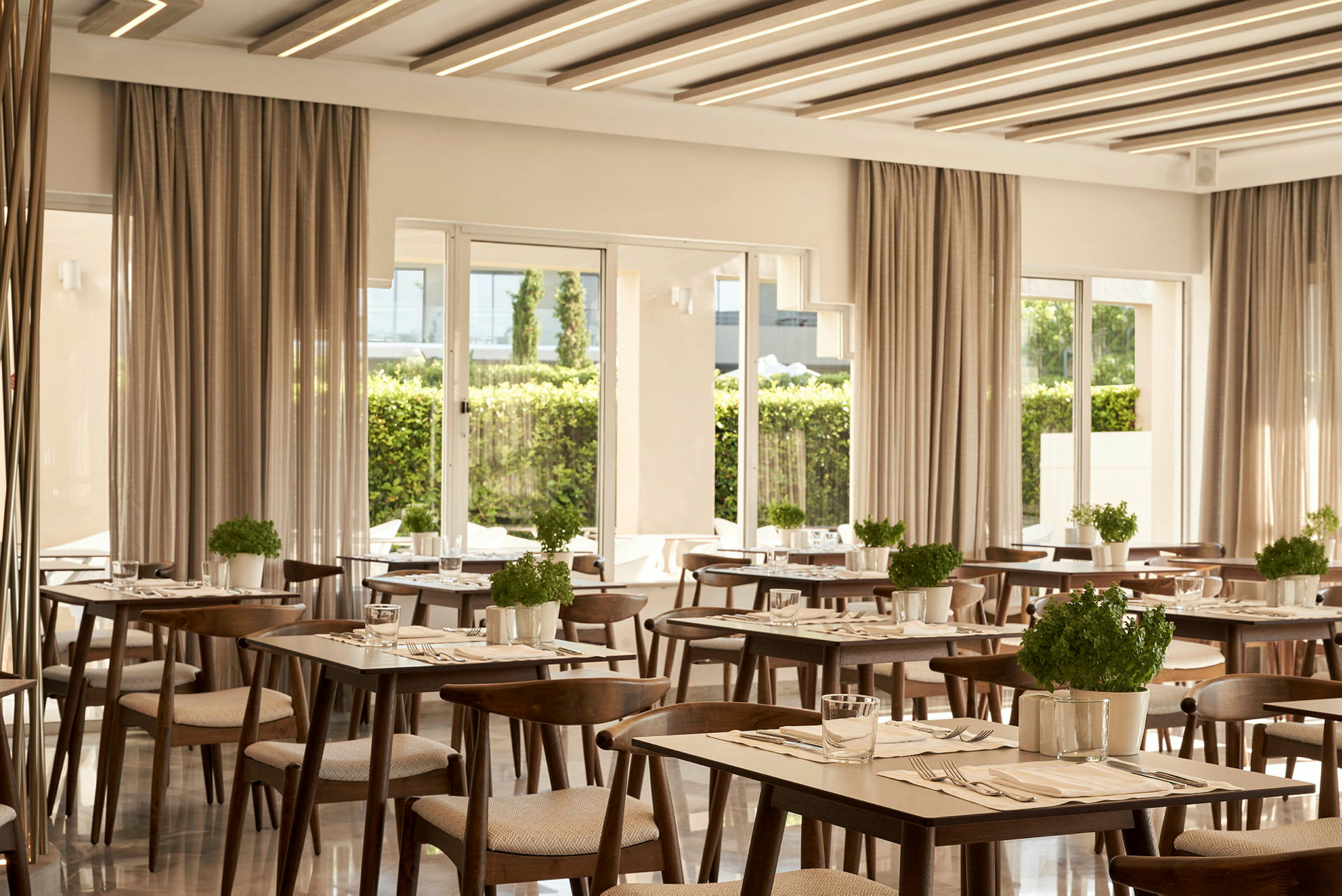 Ett modernt inrett restaurangområde med bord och stolar i trä samt planterade örtkrukor. (AI-genererad text)
