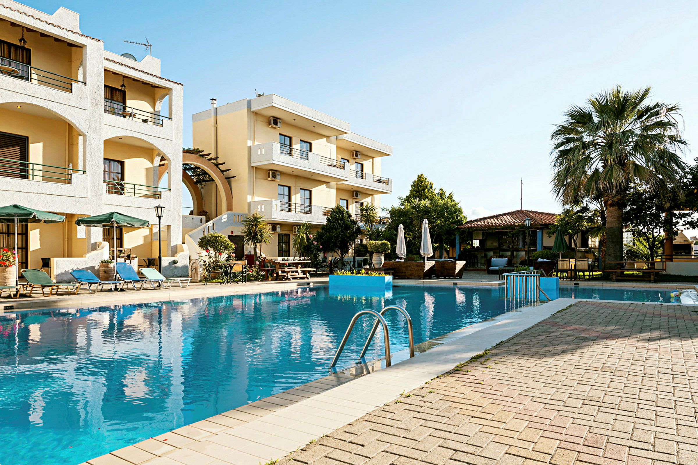 Vy över en pool omgiven av solstolar och ett hotell i bakgrunden. (AI-genererad text)