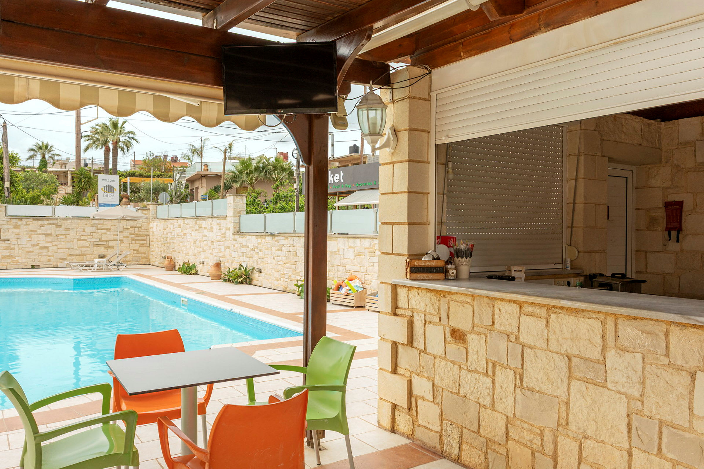 Utomhusområde med swimmingpool, bord och stolar samt en bar med stenfasad. (AI-genererad text)
