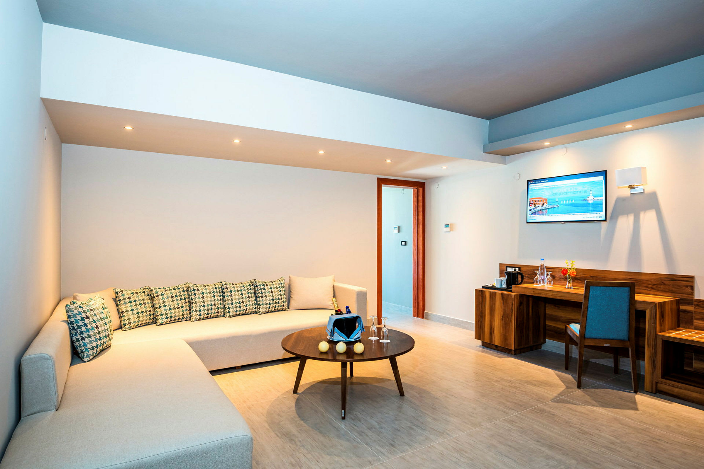 Ett modernt vardagsrum med beige soffa, soffbord, skrivbord och väggmonterad TV. (AI-genererad text)