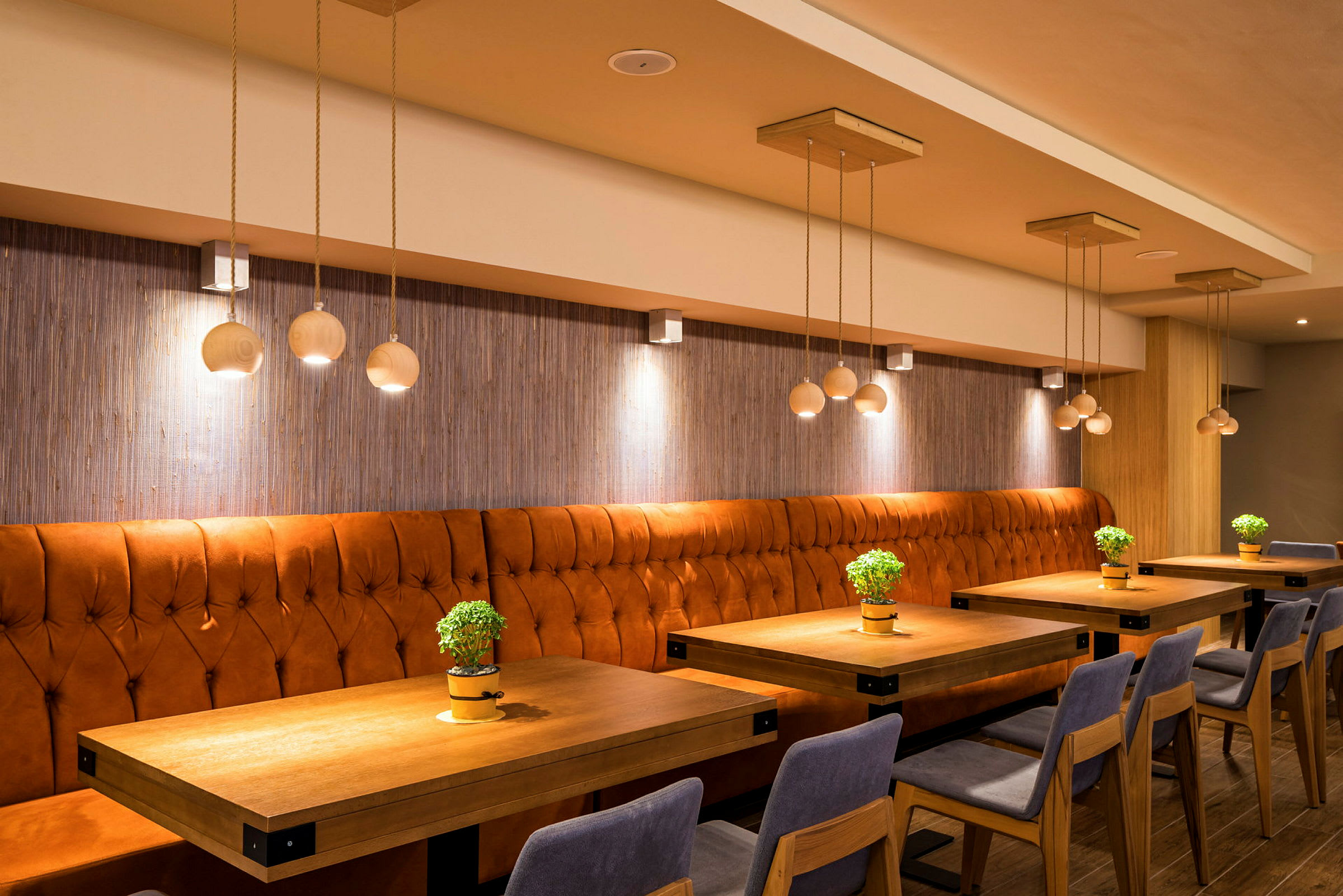 Interiör av en restaurang med orange stoppade bänkar och bord dekorerade med små gröna växter. (AI-genererad text)