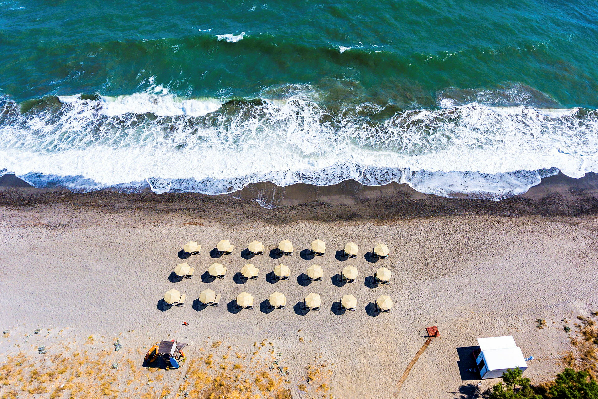 Flygfoto av en strand med paraplyer och vågor. (AI-genererad text)