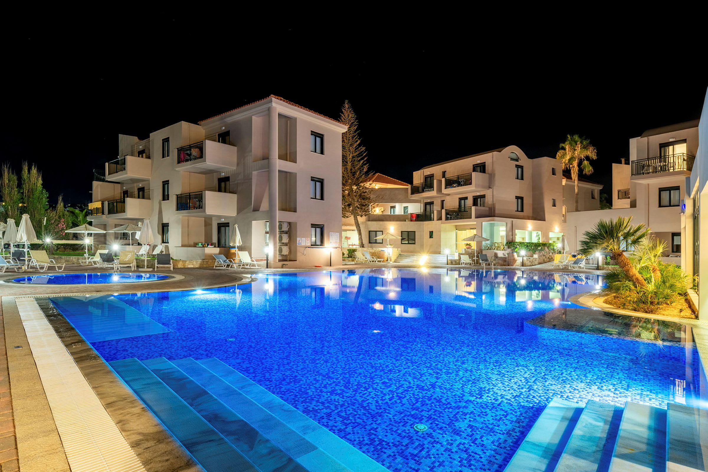 Hotellbyggnad belyst på kvällen med en swimmingpool i förgrunden. (AI-genererad text)