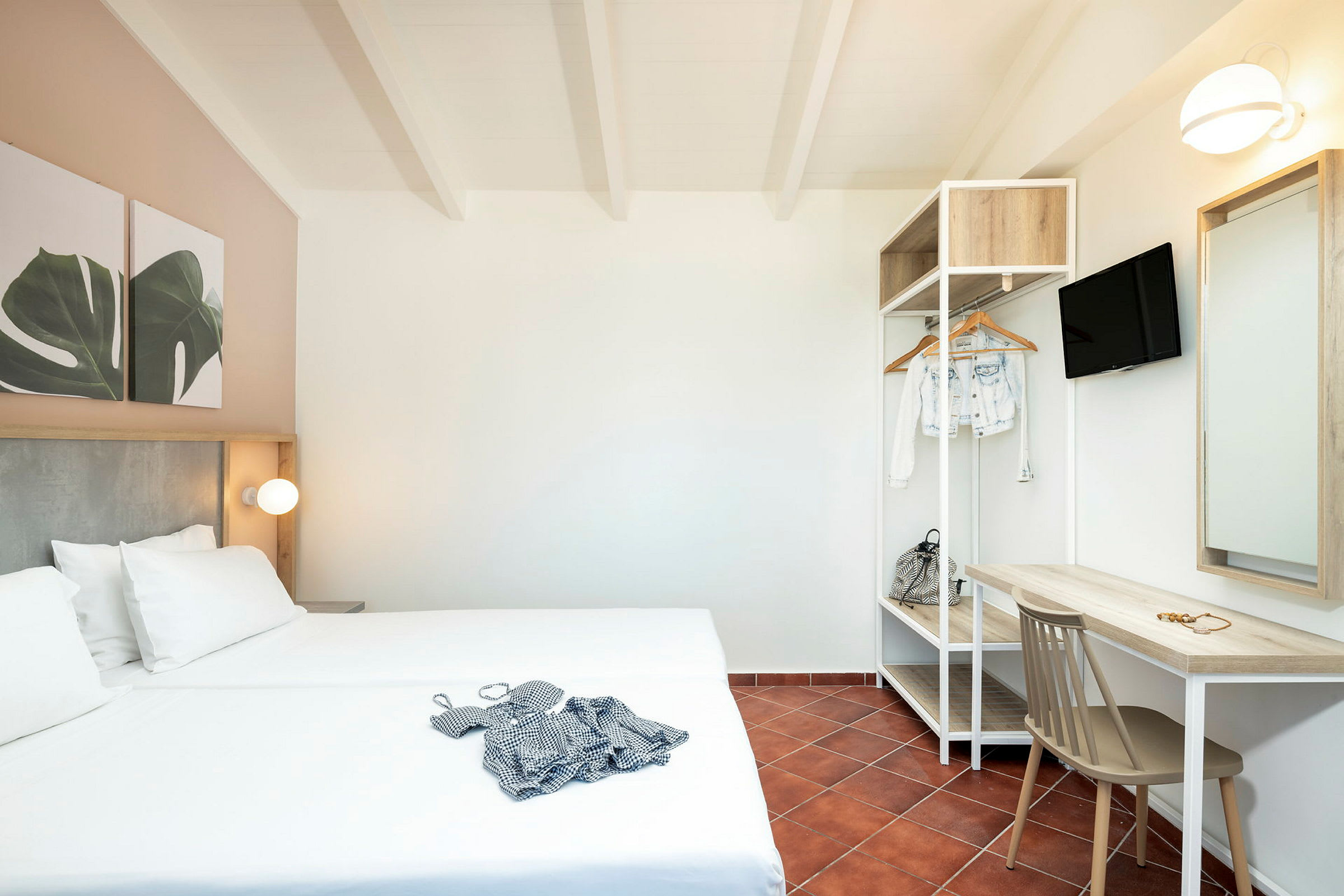 Ett hotellrum med en dubbelsäng, skrivbord, stol och öppet klädställ. (AI-genererad text)