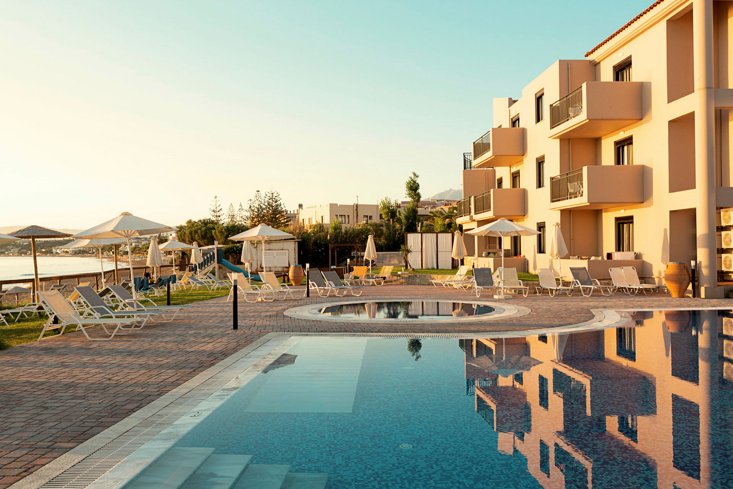 En pool med solstolar och parasoller nära en byggnad i ett soligt område. (AI-genererad text)