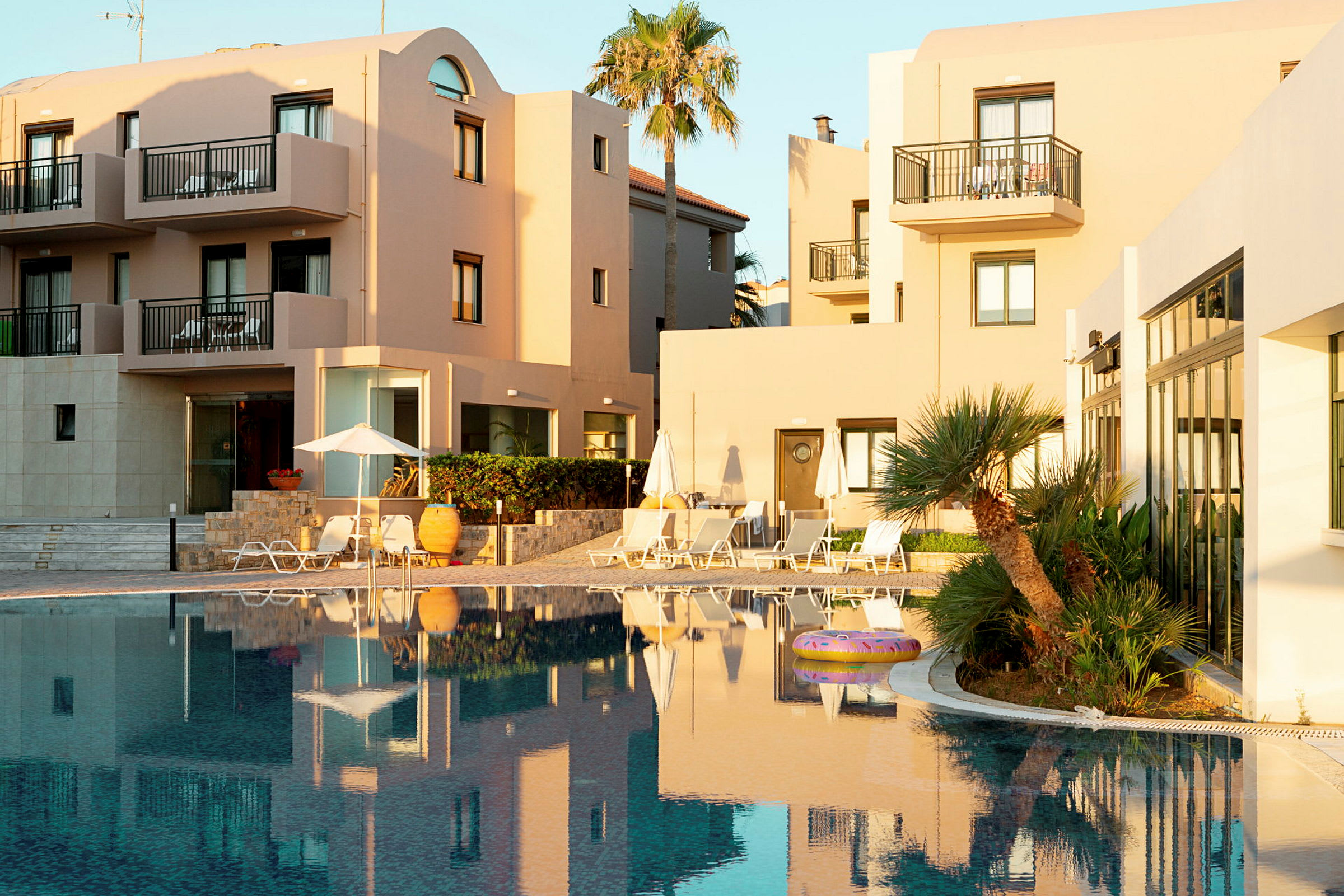 Hotellbyggnader vid en pool med palmer och solstolar. (AI-genererad text)
