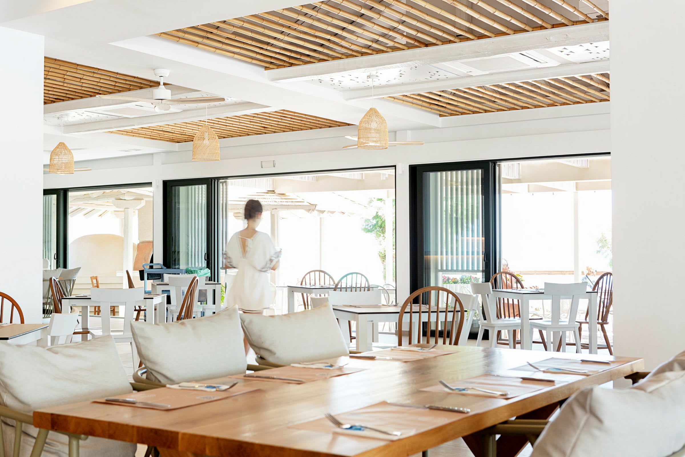 Bilden visar en restaurangmiljö med tomma bord, stolar och en person i rörelse i bakgrunden. (AI-genererad text)