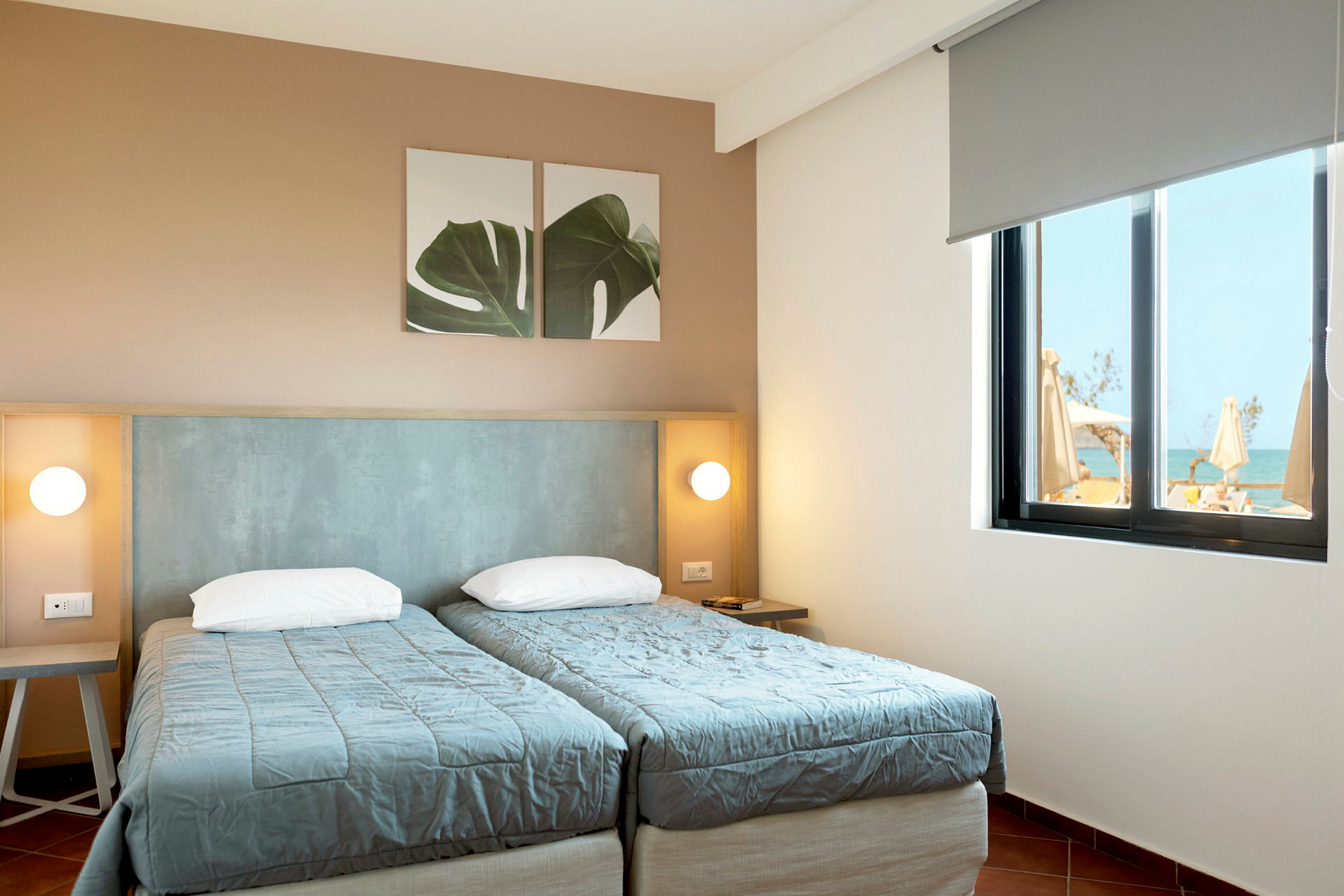 Två enkelsängar i ett hotellrum med en väggdekoration och fönster med utsikt. (AI-genererad text)