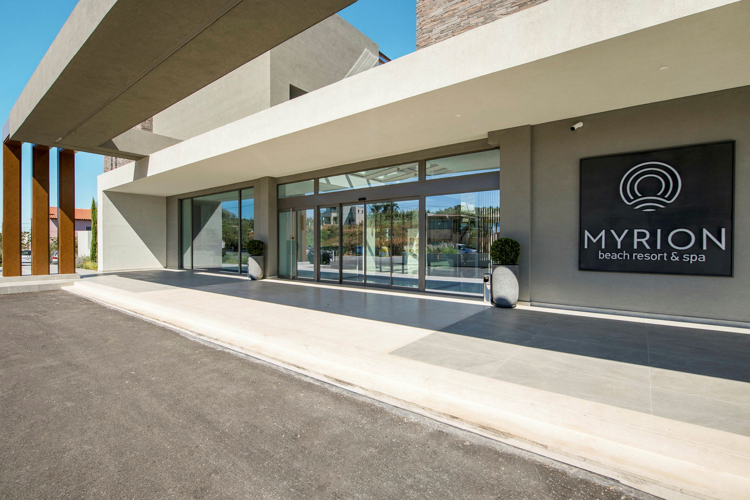 Entrén till Myrion Beach Resort & Spa med glasväggar och en skylt. (AI-genererad text)
