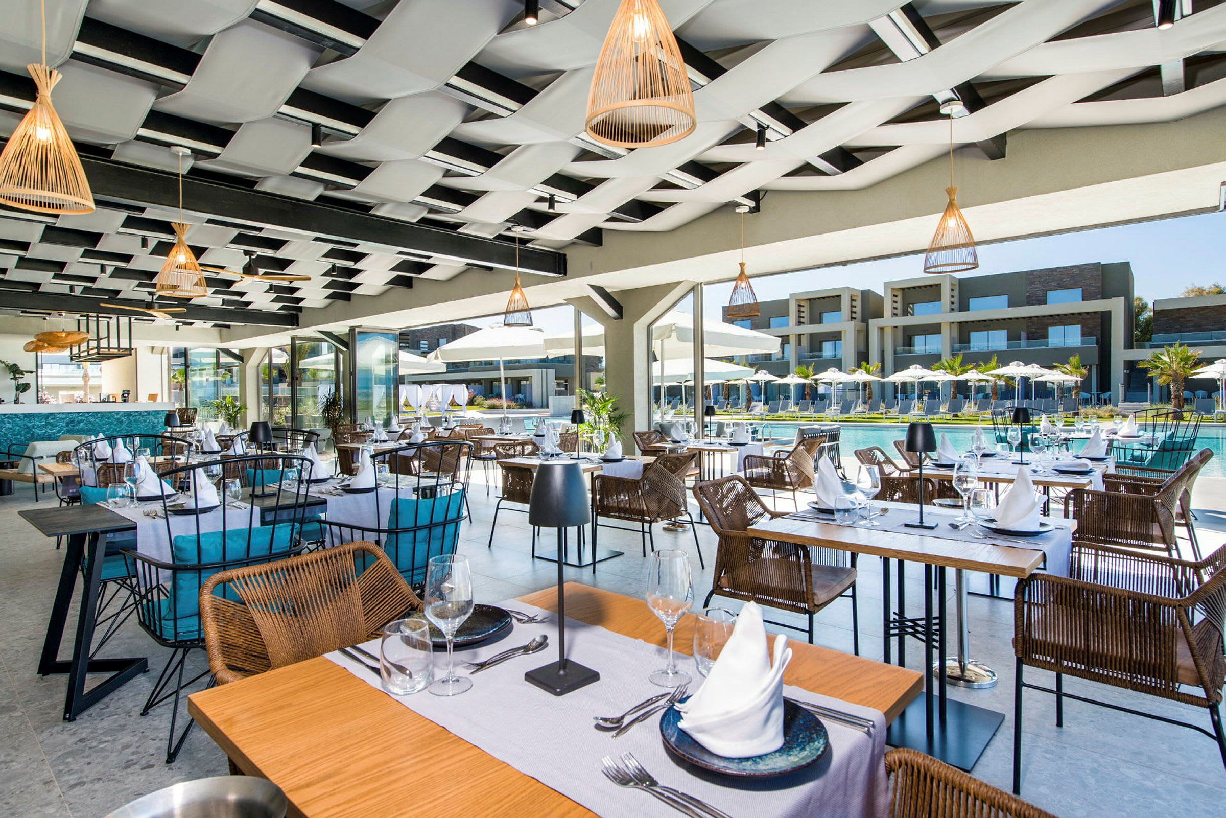 Restaurang med bord och stolar nära en pool, med resortbyggnader i bakgrunden. (AI-genererad text)