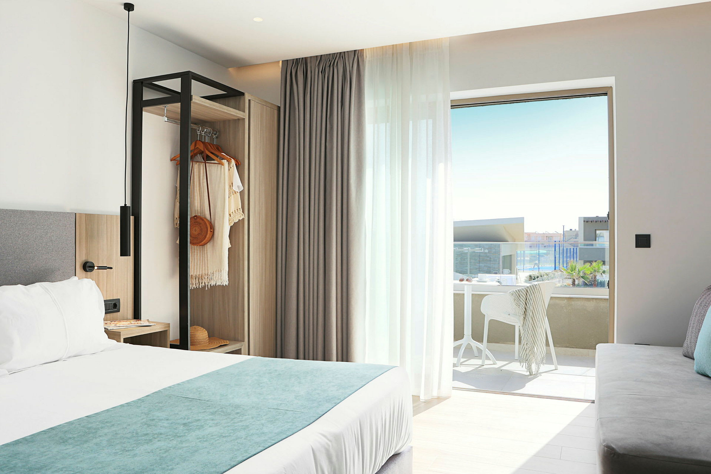 Ett hotellrum med en dubbelsäng, en öppen garderob och en möblerad balkong med utsikt. (AI-genererad text)