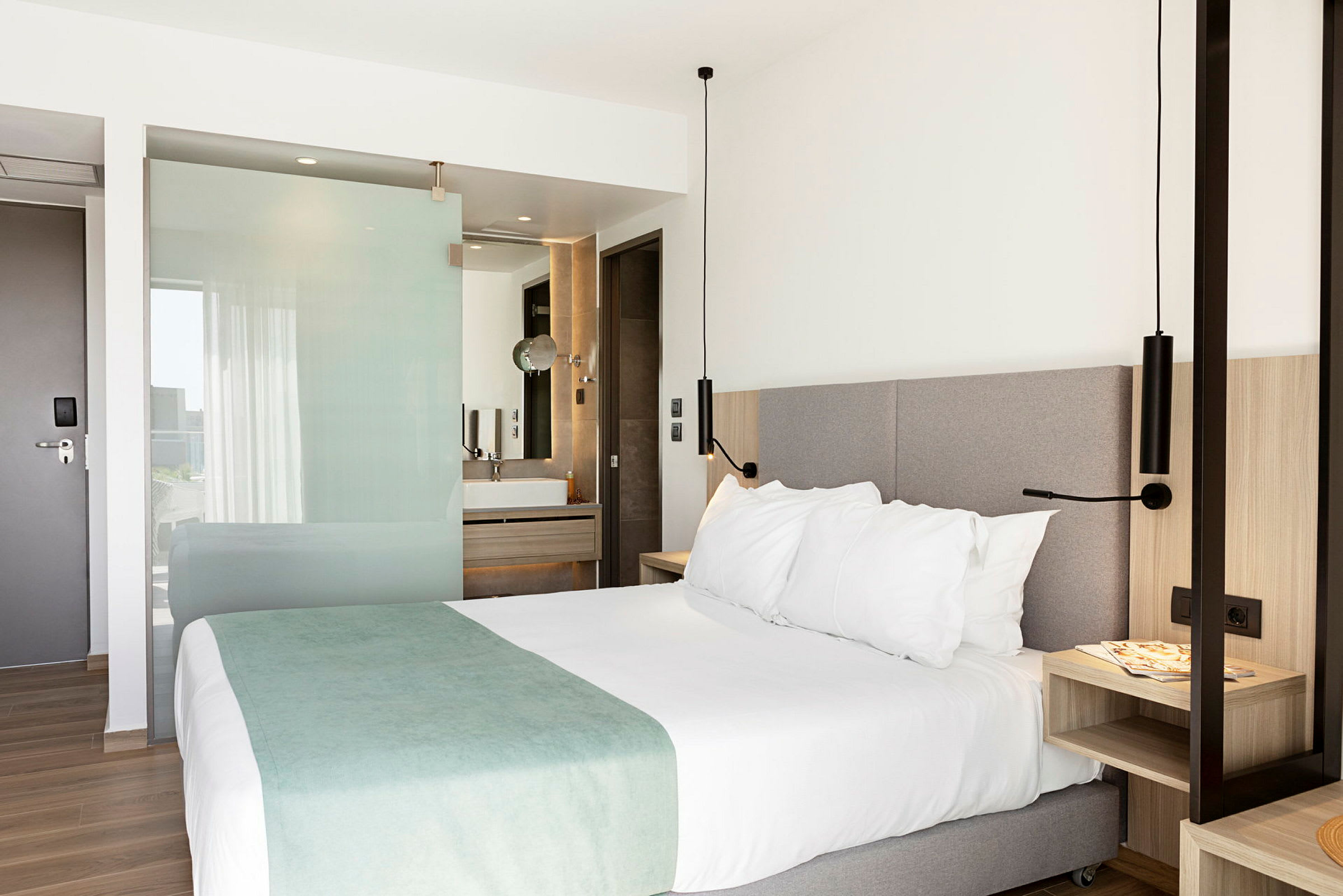 Hotelrum med en dubbelsäng, nattygsbord och öppen planlösning mot badrum. (AI-genererad text)