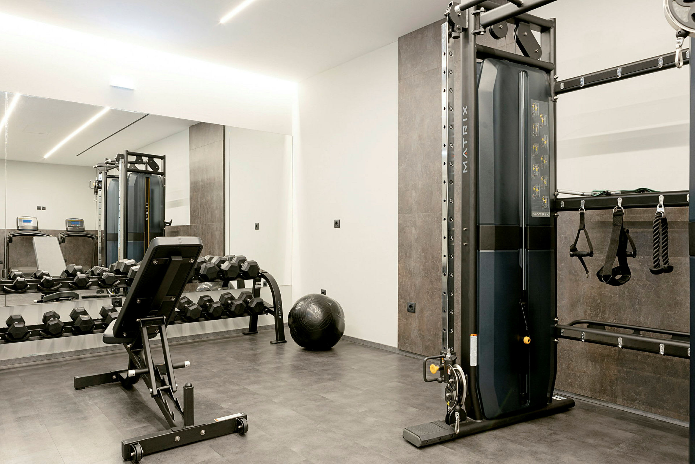 Ett gym med träningsutrustning, inklusive hantlar, en bänkpress och en träningsmaskin. (AI-genererad text)