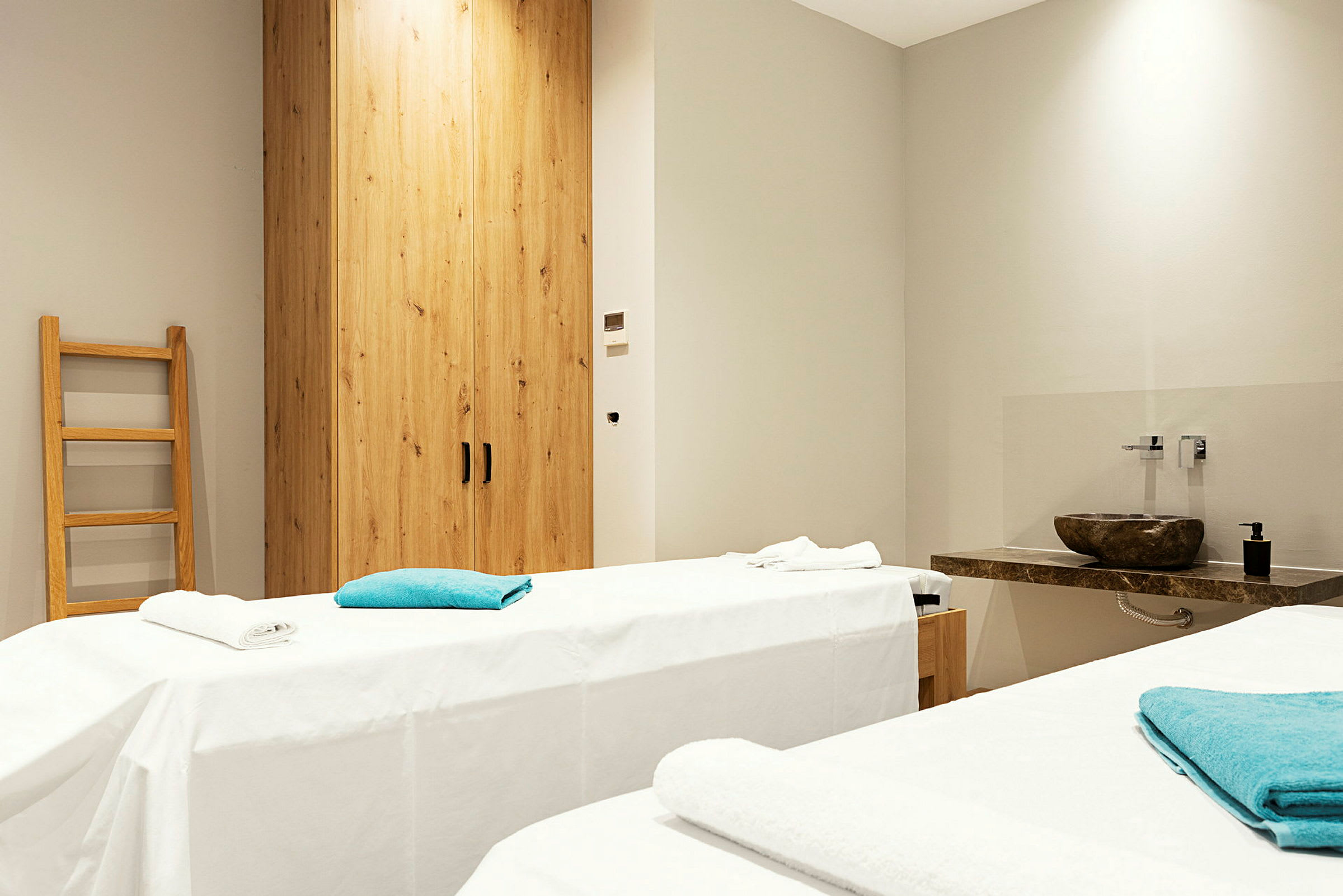 Rum med två massagebänkar täckta med vita dukar och blå handdukar. (AI-genererad text)