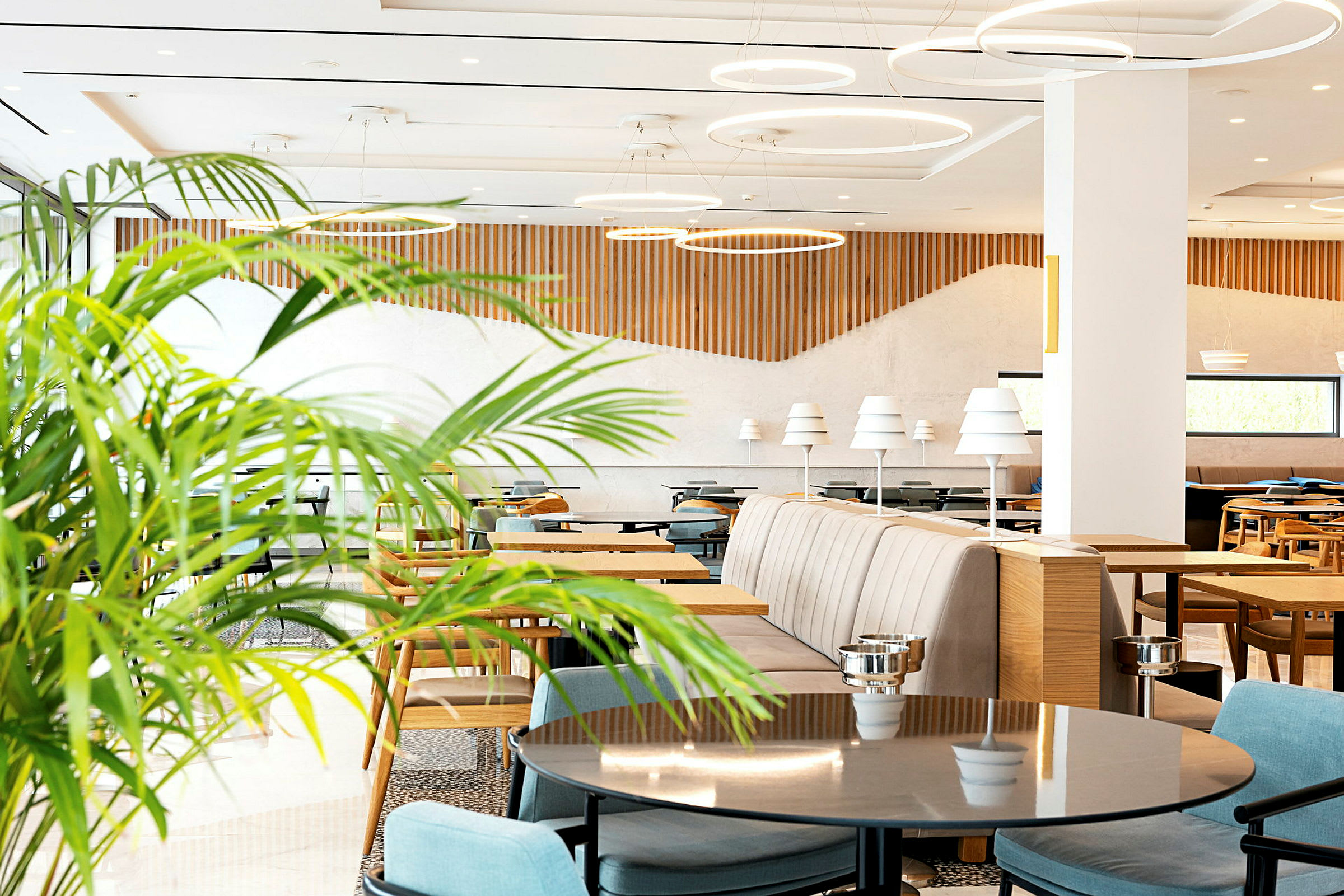 Ljus och modern restaurang med bord, stolar och dekorativa gröna växter. (AI-genererad text)