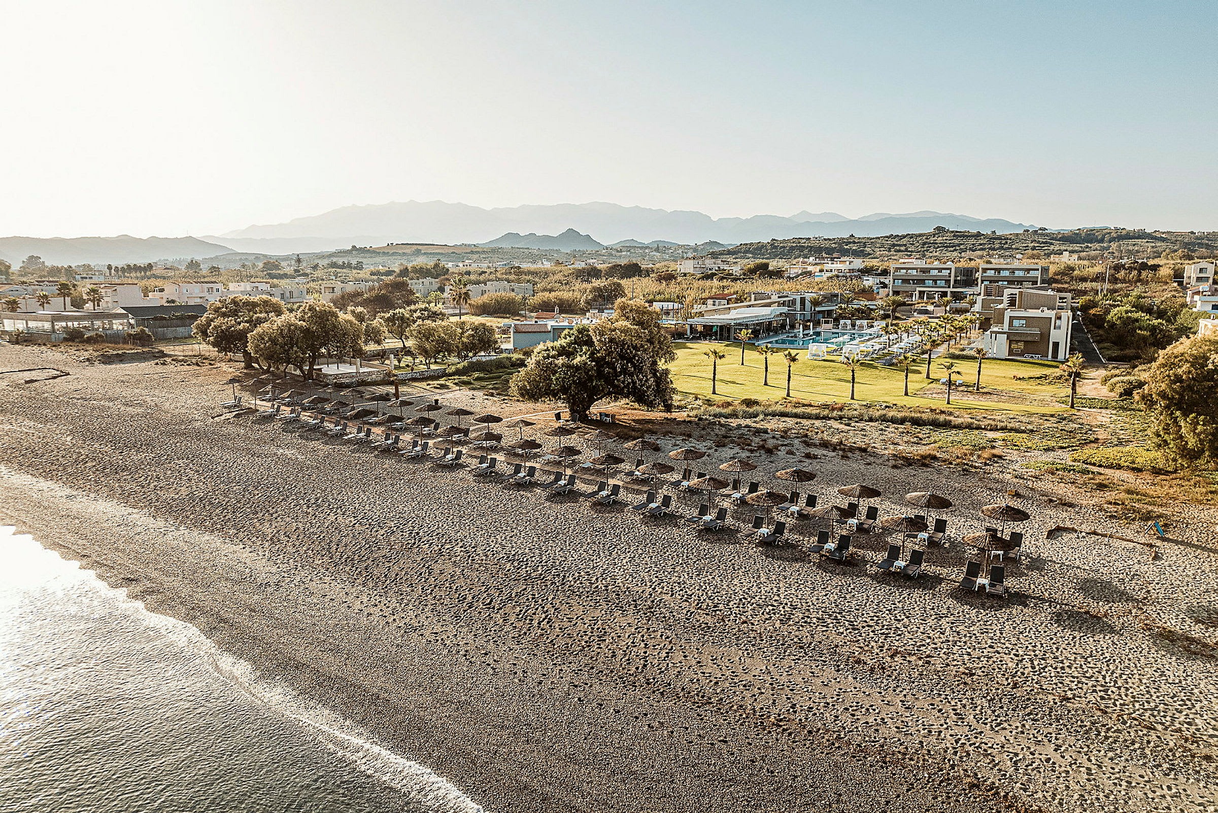 En strand med solstolar och parasoller, omgiven av grönska och hotellbyggnader i bakgrunden. (AI-genererad text)