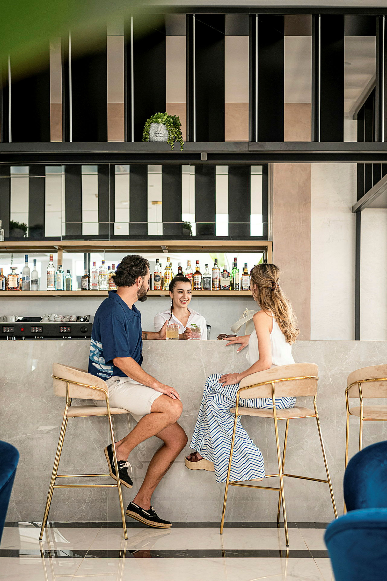 Bild av två personer sittande vid en marmordisk på en modern bar med hyllor fyllda med flaskor. (AI-genererad text)