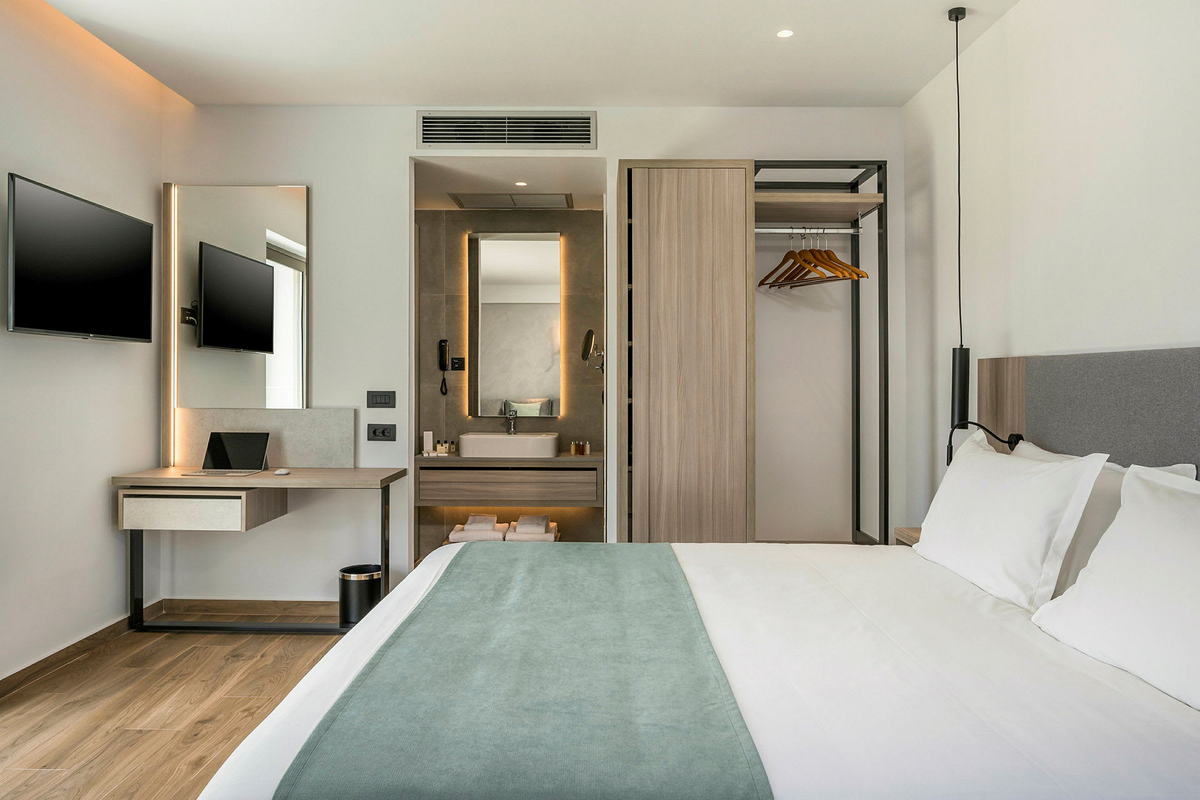 Modernt hotellrum med dubbelsäng, arbetsbord med TV samt en öppen garderob och badrum. (AI-genererad text)