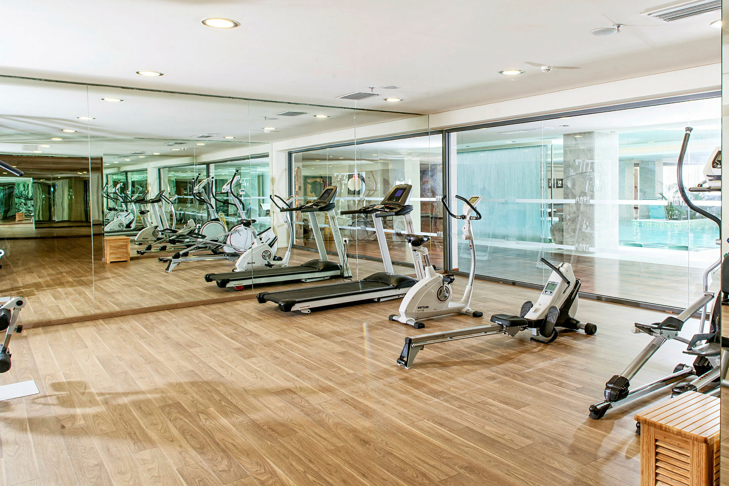 Ett gym med träningsmaskiner inklusive löpband, cyklar och roddmaskiner, samt spegelvägg och trägolv. (AI-genererad text)