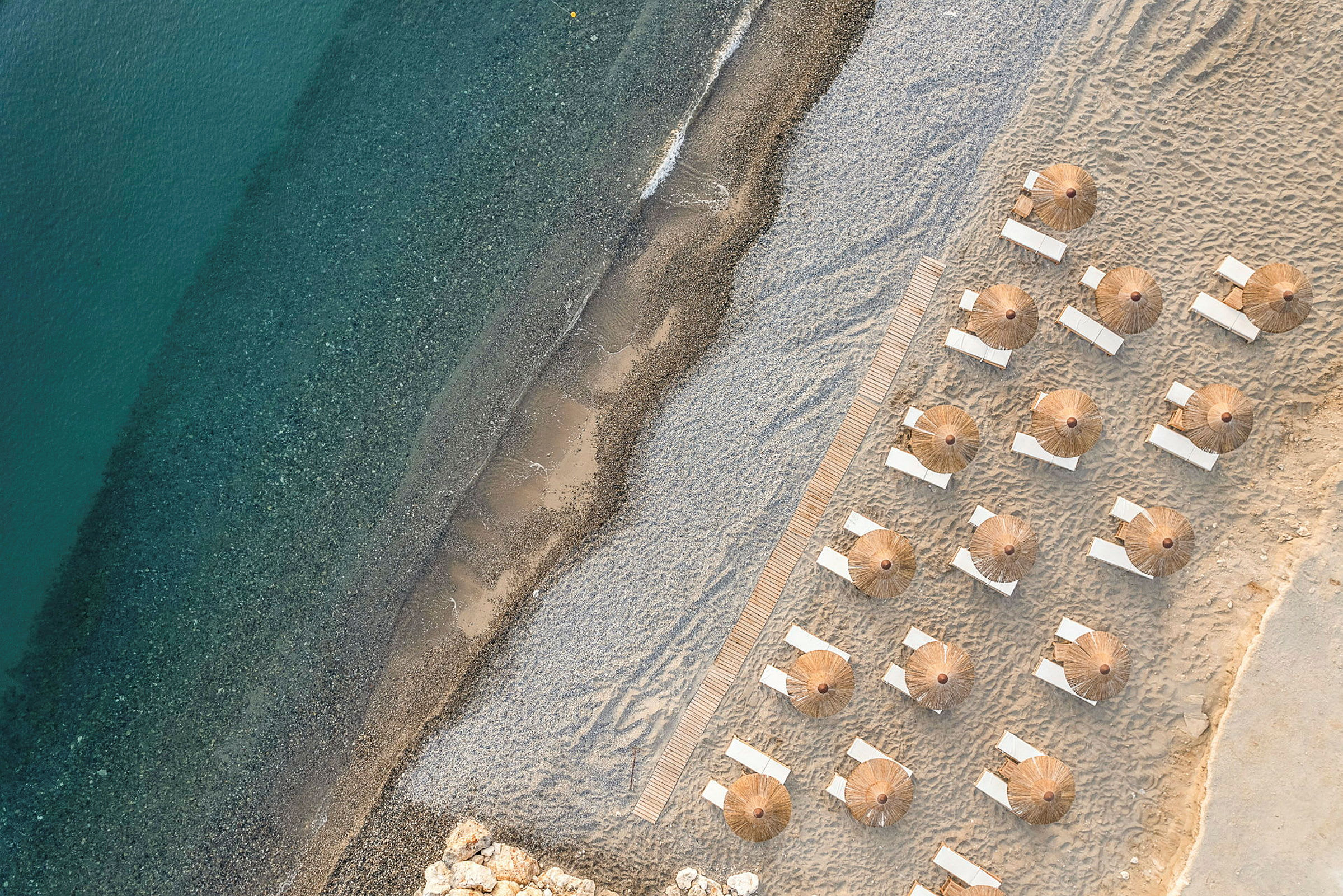 Flygbild av solstolar och parasoller uppställda på en sandstrand nära vatten. (AI-genererad text)