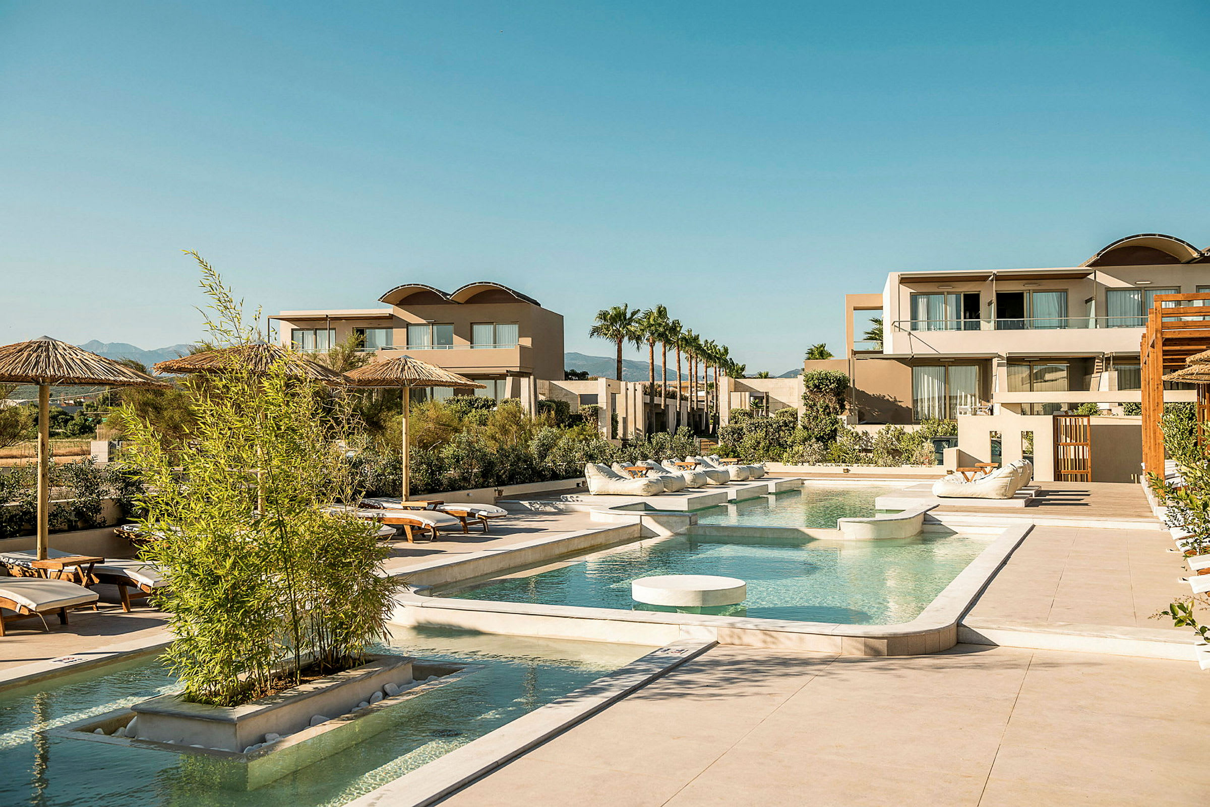 Ett hotellområde med pool och solstolar, omgiven av palmer och moderna byggnader. (AI-genererad text)