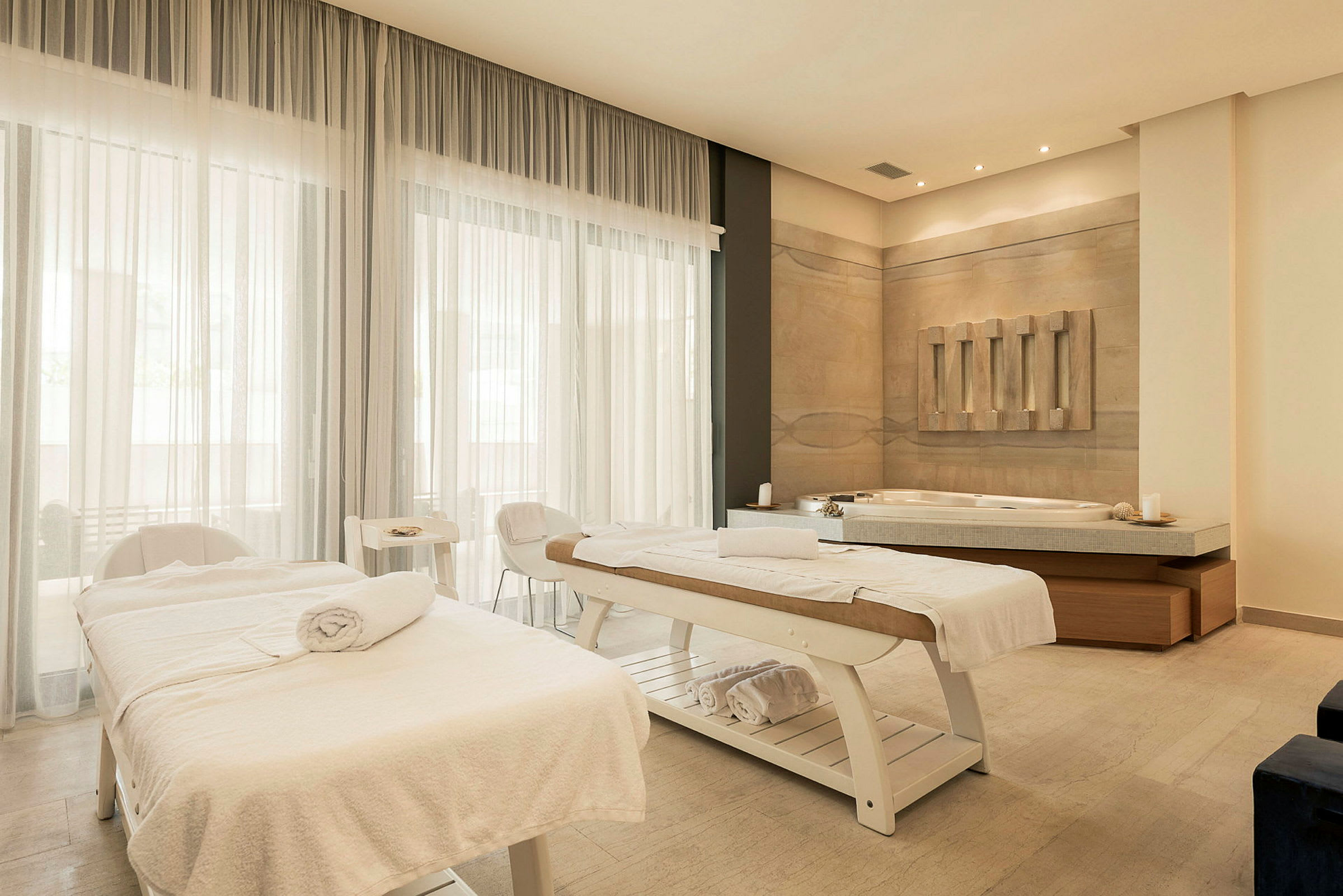 Ett massage- och spabehandlingsrum med två britsar, vita handdukar och en jacuzzi i en lugnande miljö. (AI-genererad text)