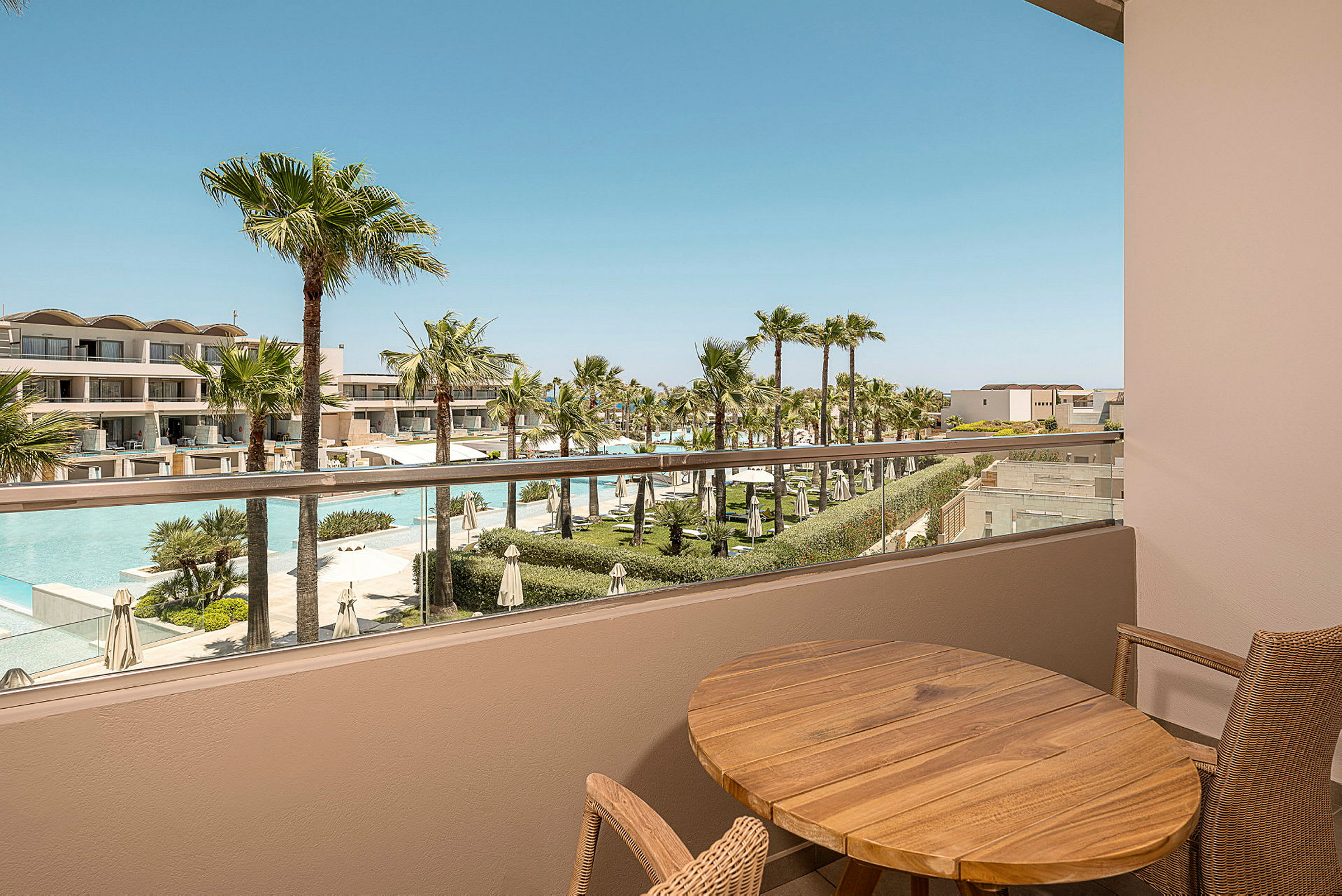 Utsikt från en balkong över en resort med palmer och pooler. (AI-genererad text)