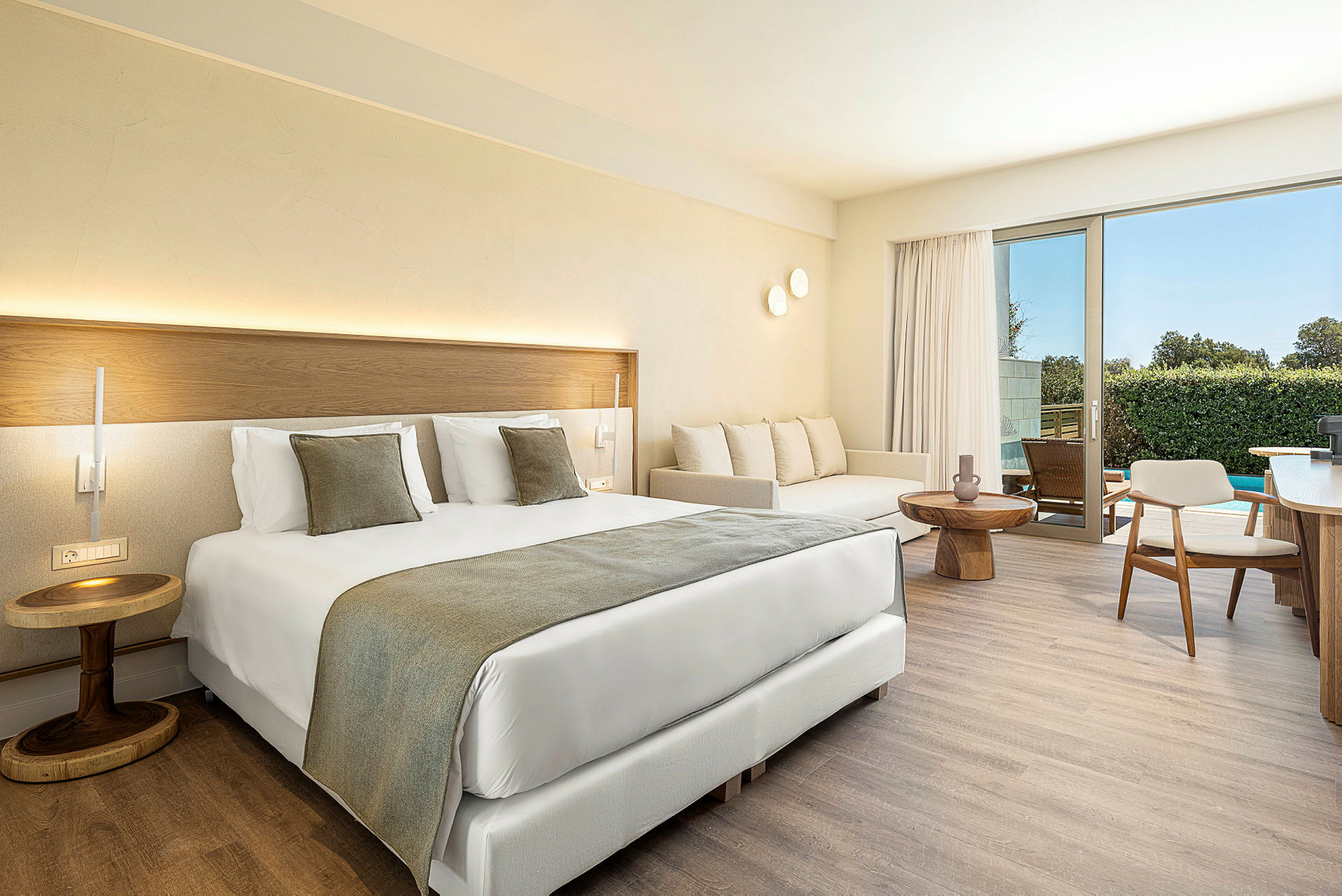 Ett modernt hotellrum med en stor säng, soffa och ett bord. Rummet har ljusa väggar och en balkong med utsikt. (AI-genererad text)