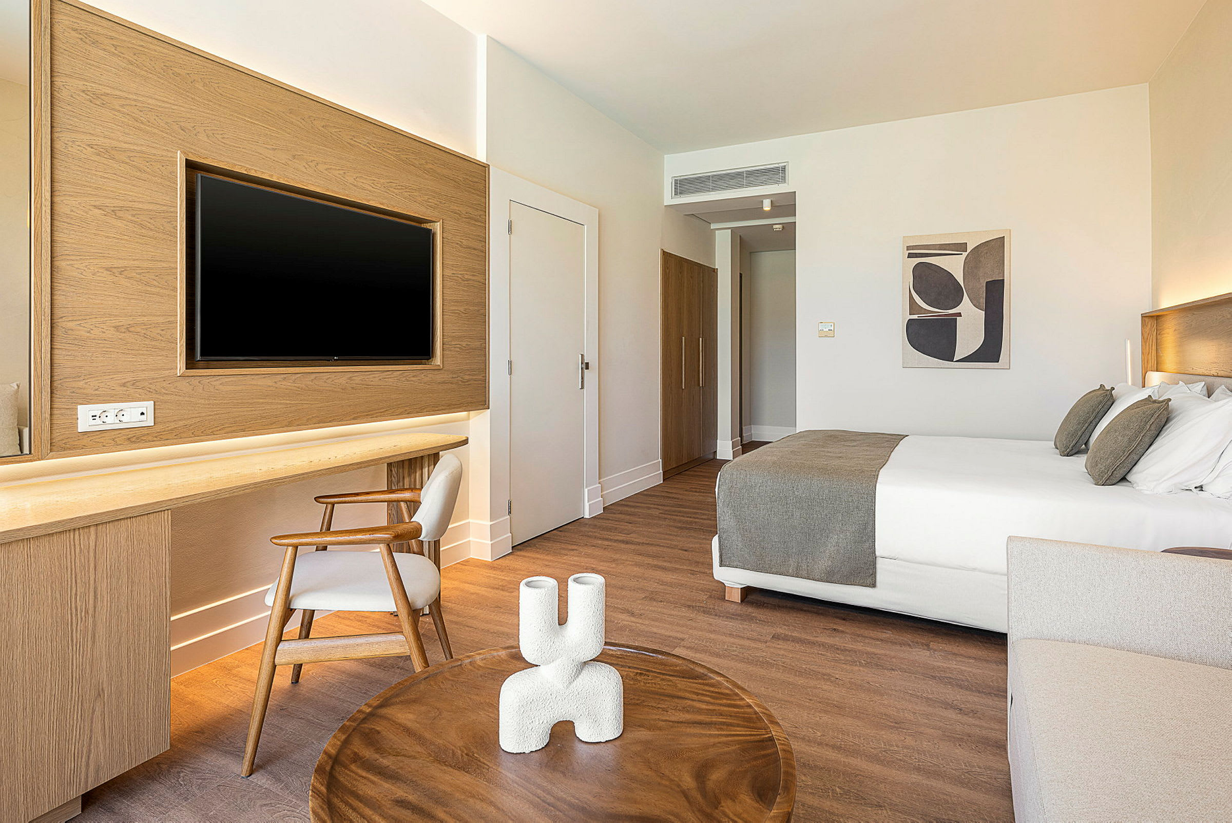 Ett modernt hotellrum med en dubbelsäng, ett skrivbord med stol och en TV på väggen. Ett litet bord står i förgrunden. (AI-genererad text)