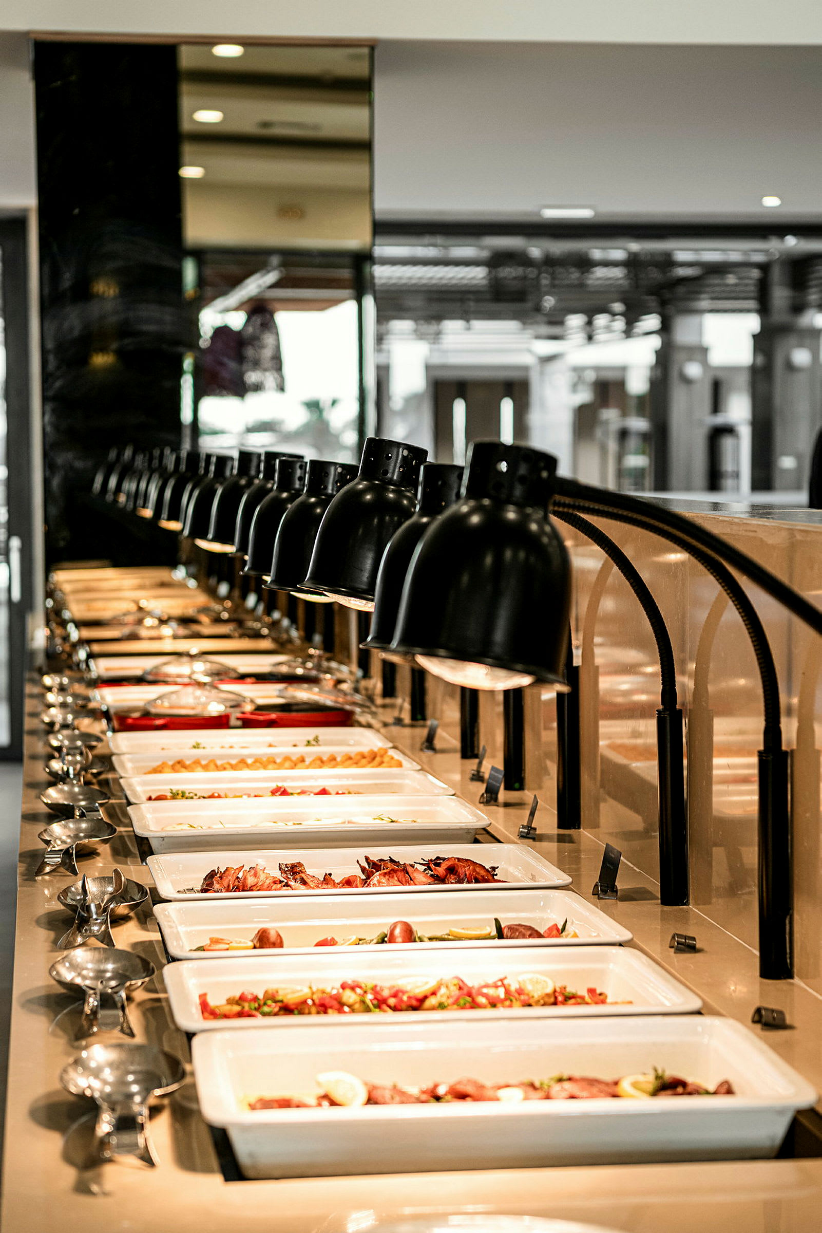 Ett buffébord med olika maträtter presenterade i rektangulära vita tallrikar under rader av lampor. (AI-genererad text)