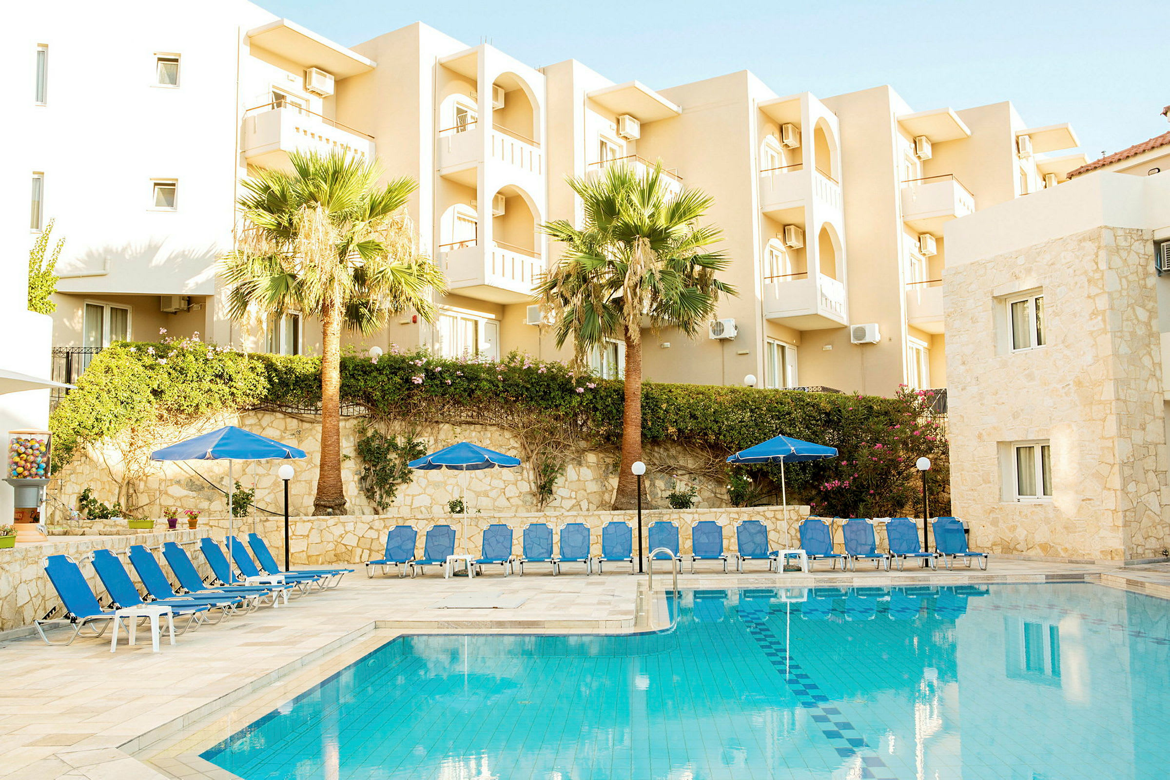 Hotellbyggnad med balkonger bredvid en pool, solstolar och parasoll. (AI-genererad text)