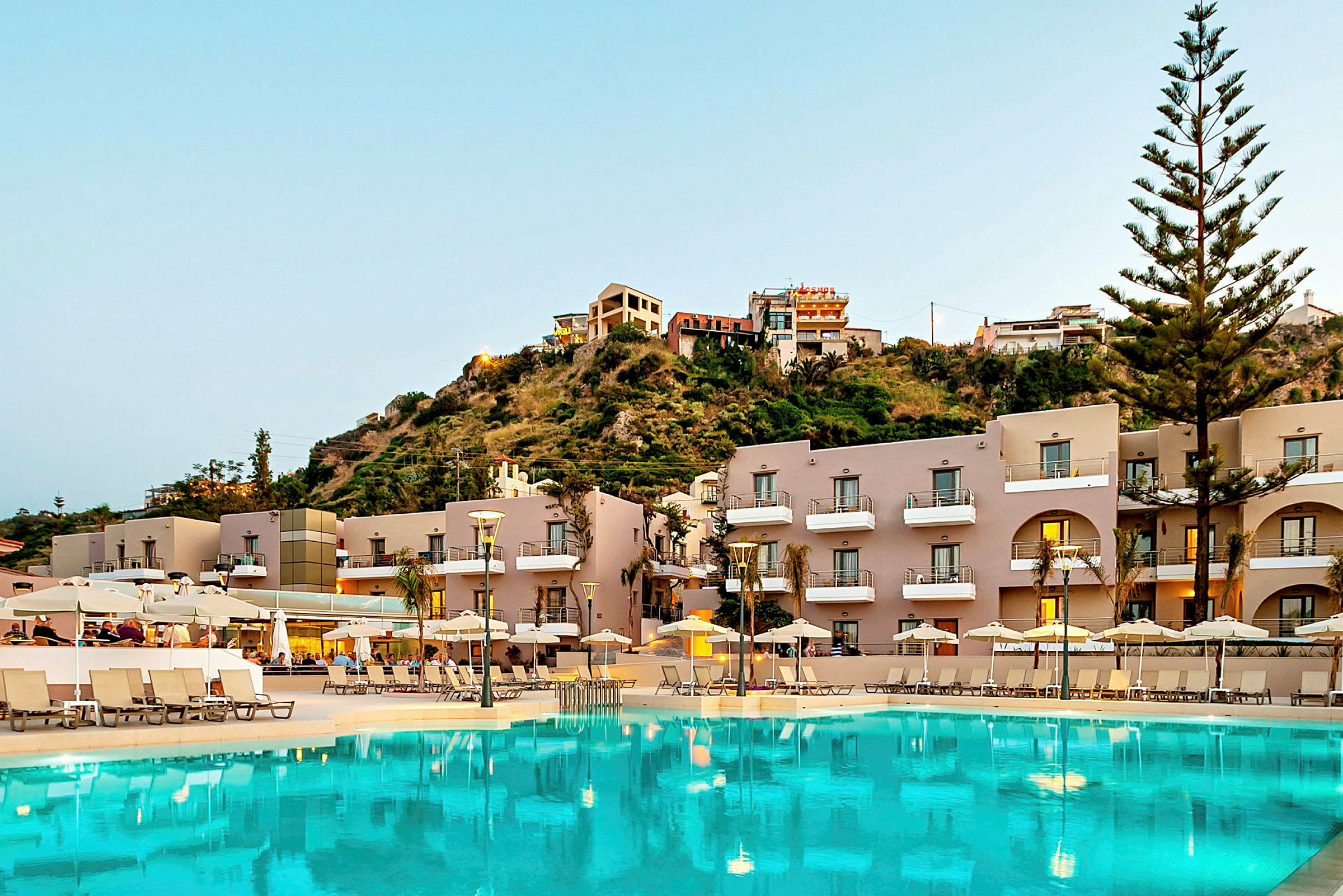 Hotellfasad med pool och solsängar framför en bergssluttning. (AI-genererad text)