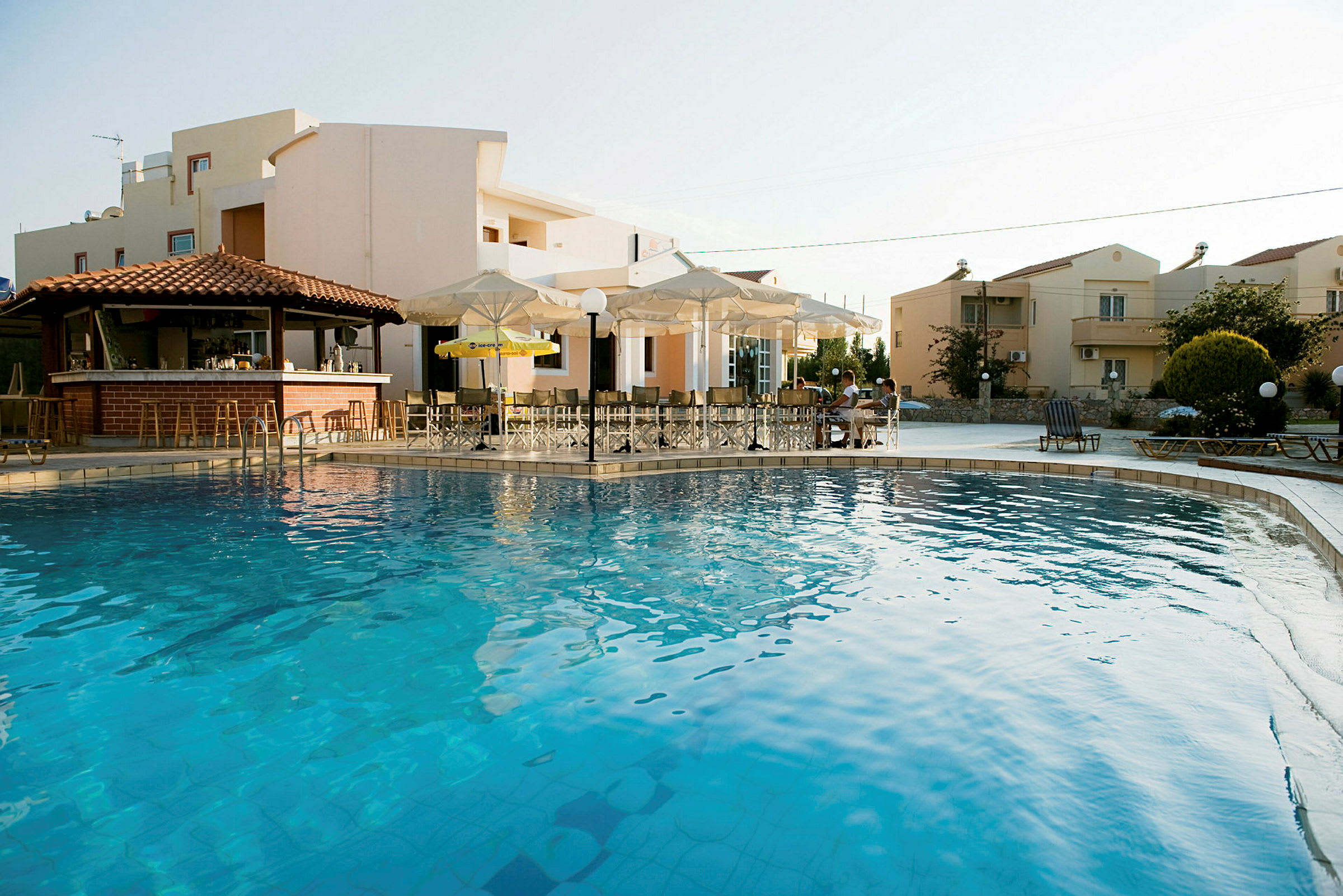 En swimmingpool framför byggnader med bar och parasoller. (AI-genererad text)