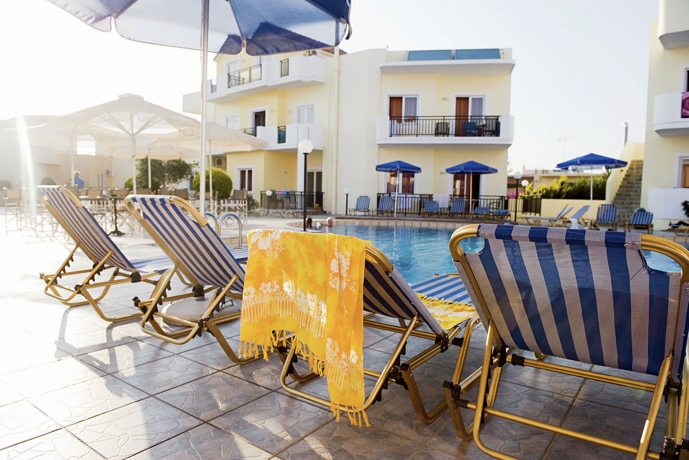 Solstolar vid en pool med gula bostadshus i bakgrunden. (AI-genererad text)