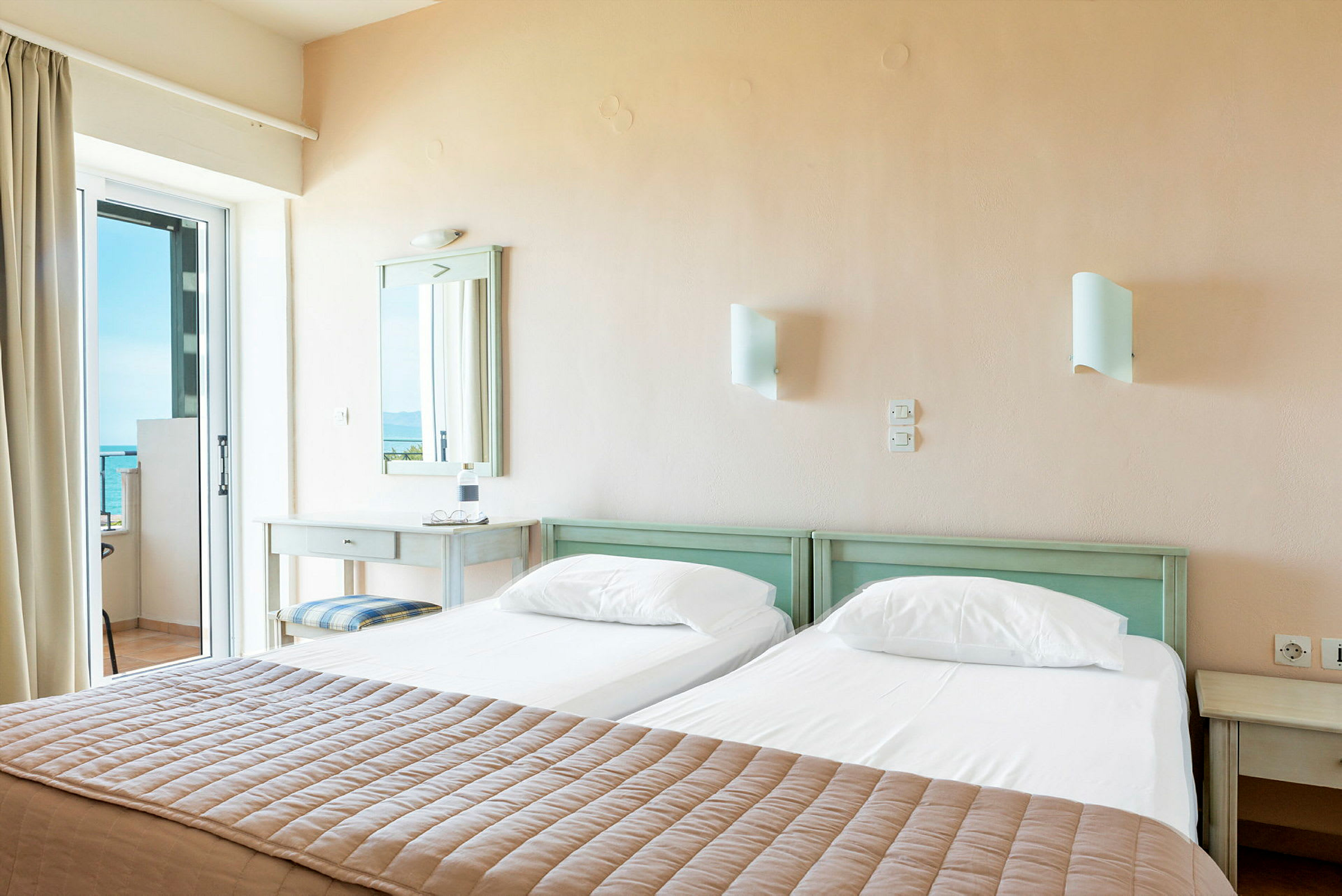 Ett hotellrum med två enkelsängar och utsikt över havet genom en glasdörr. (AI-genererad text)